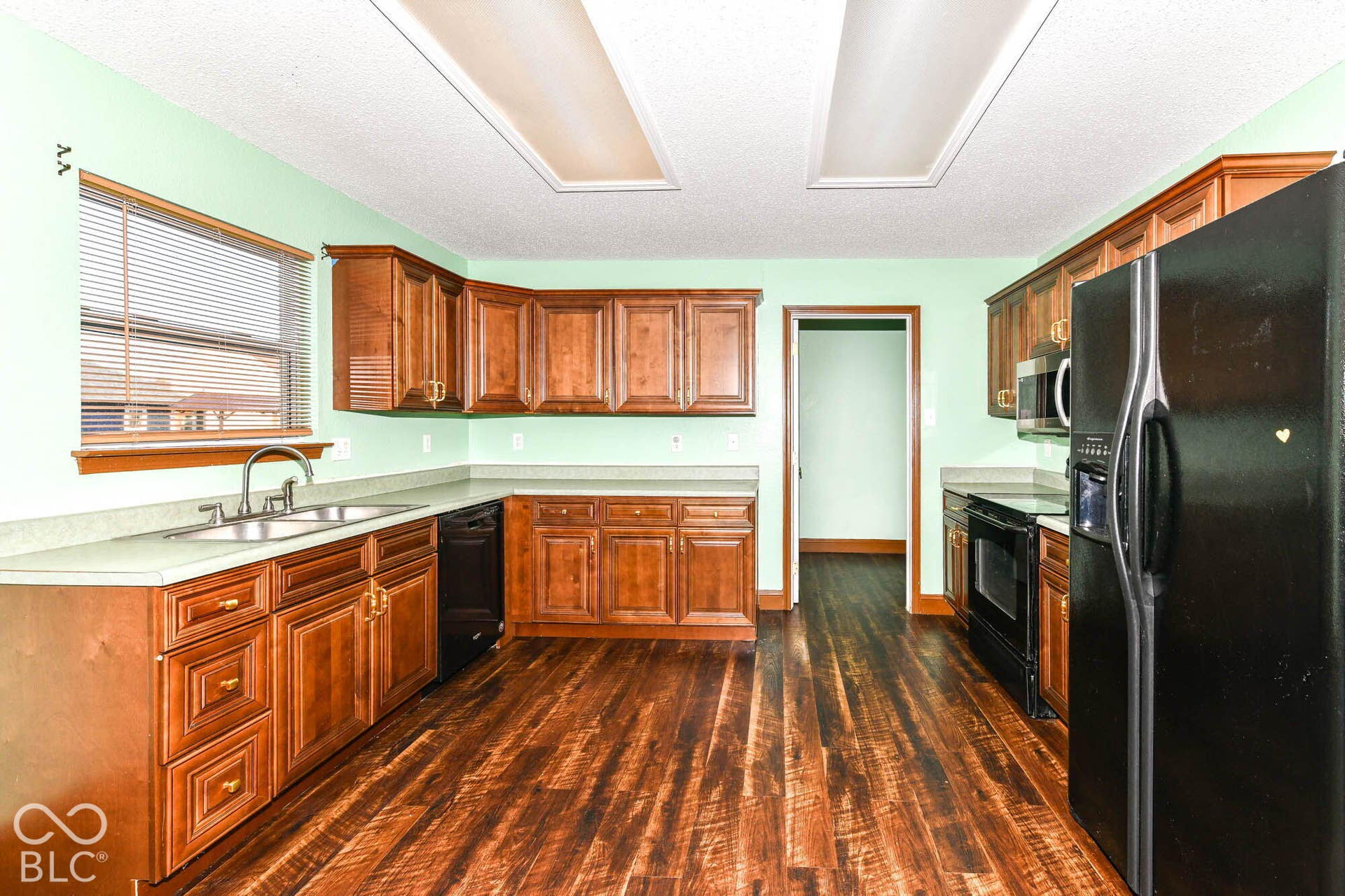 Kitchen featuring wood-finish flooring, ample wood cabinetry, a double basin sink, and counter space