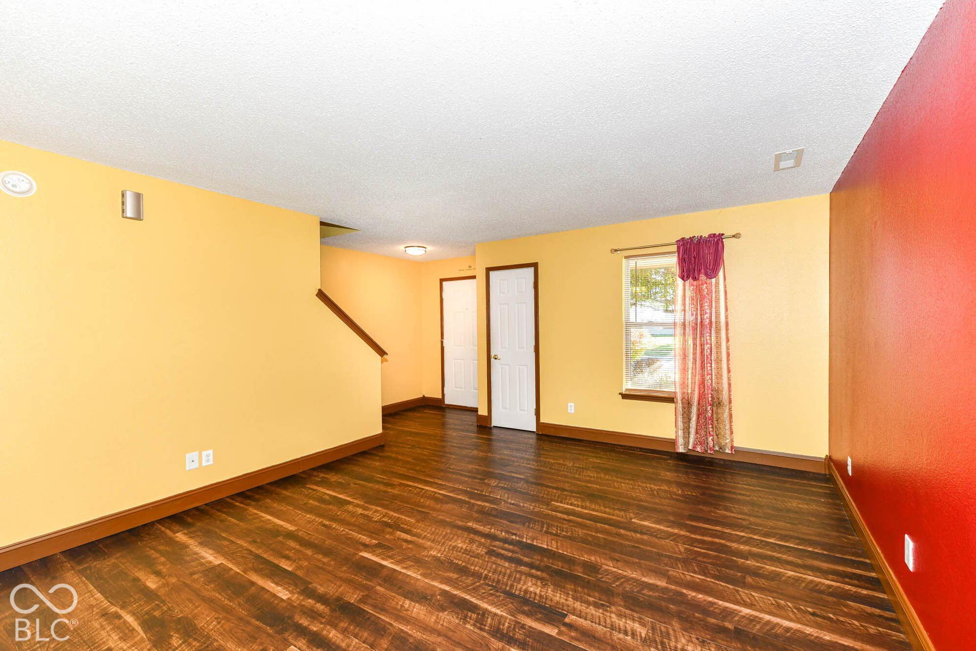 Wood-finish flooring, a prominent window, a staircase with a wood handrail, and white interior doors