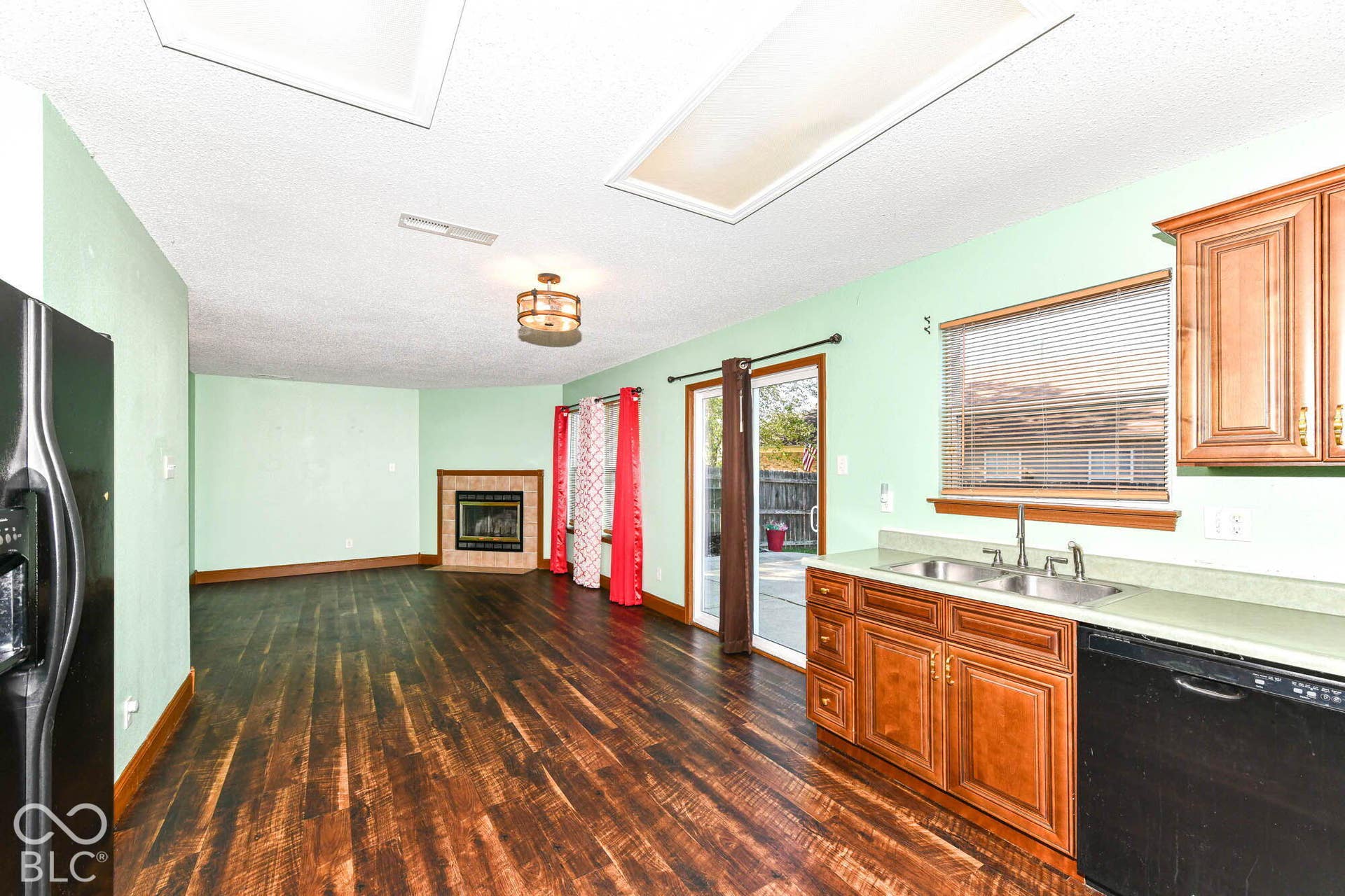 Wood-finish flooring throughout, kitchen with wood cabinetry and dual basin sink, sliding glass door access to exterior, and a built-in fireplace with a stone surround