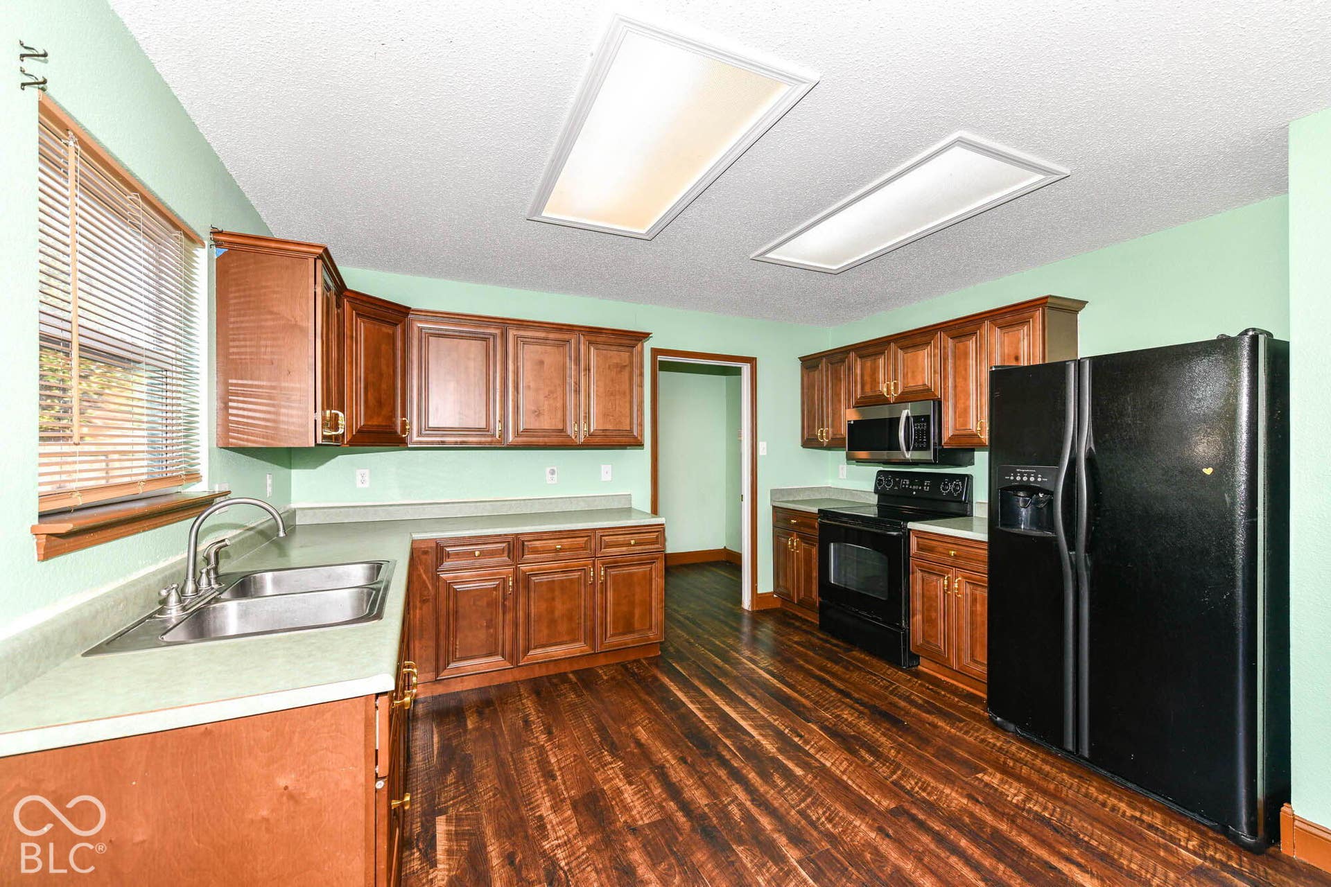 Kitchen featuring wood-finish flooring, wood cabinetry, a double basin stainless steel sink, and a black appliance package including a refrigerator, range, and microwave