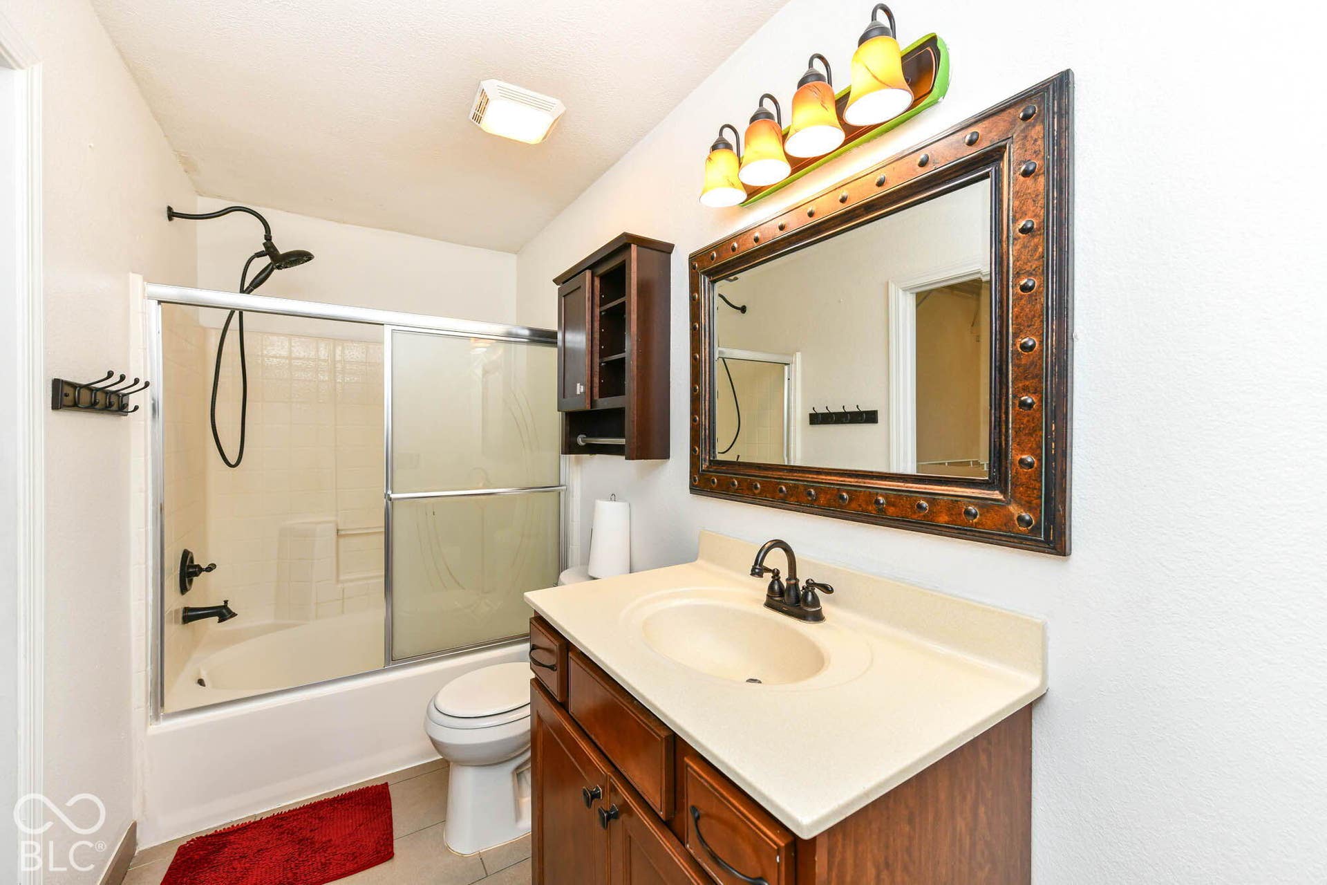 Bathroom featuring a built-in tub with sliding glass doors, a vanity with an integrated sink and base cabinetry, a wall-mounted medicine cabinet, and a framed mirror