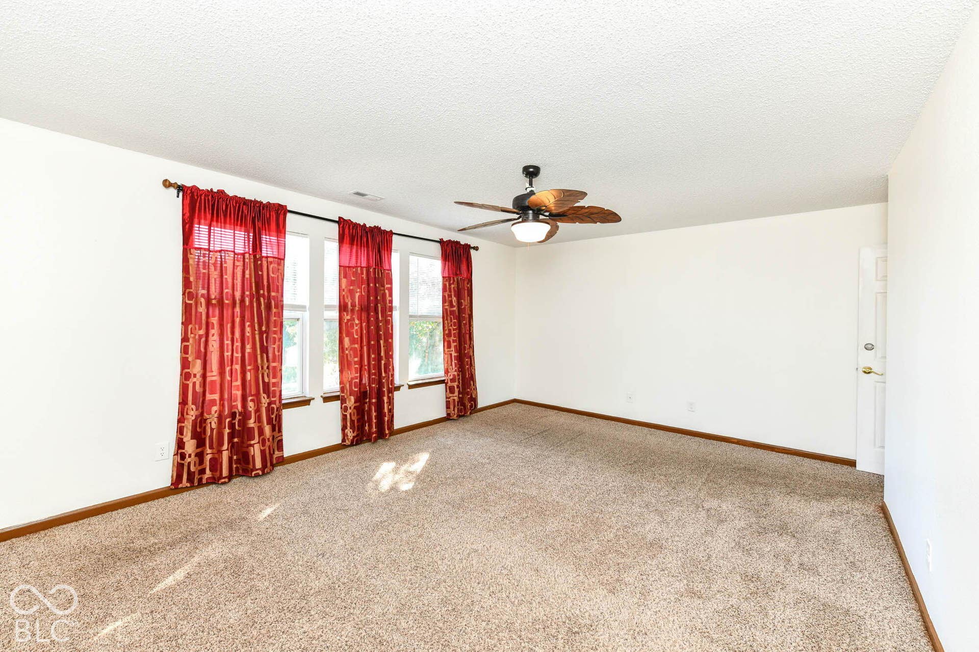 Expansive room featuring light-colored carpeting, multiple windows, and a ceiling fan with integrated lighting