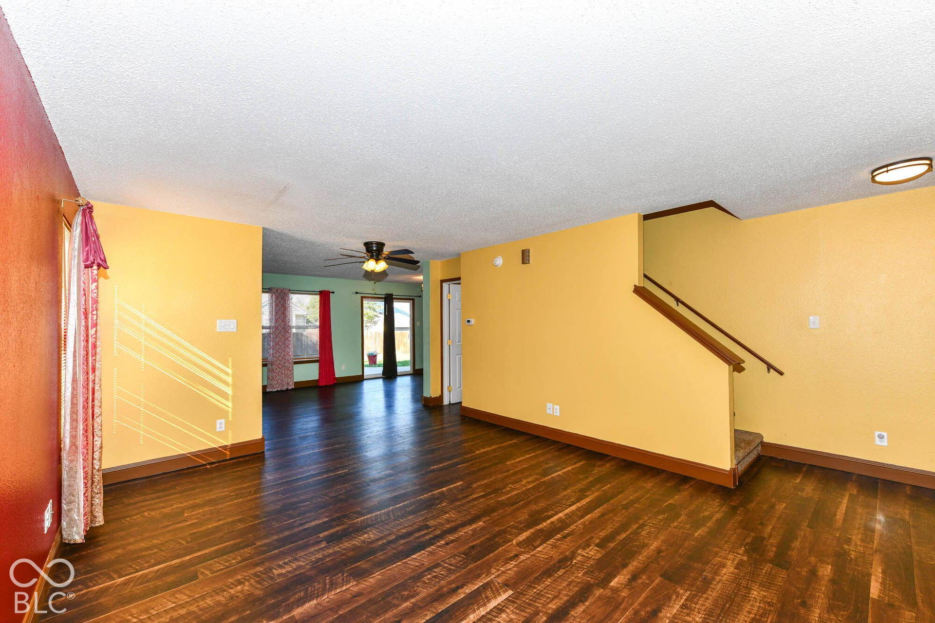 Wood-finish flooring throughout, a ceiling fan in the rear room, and a staircase with a wood handrail