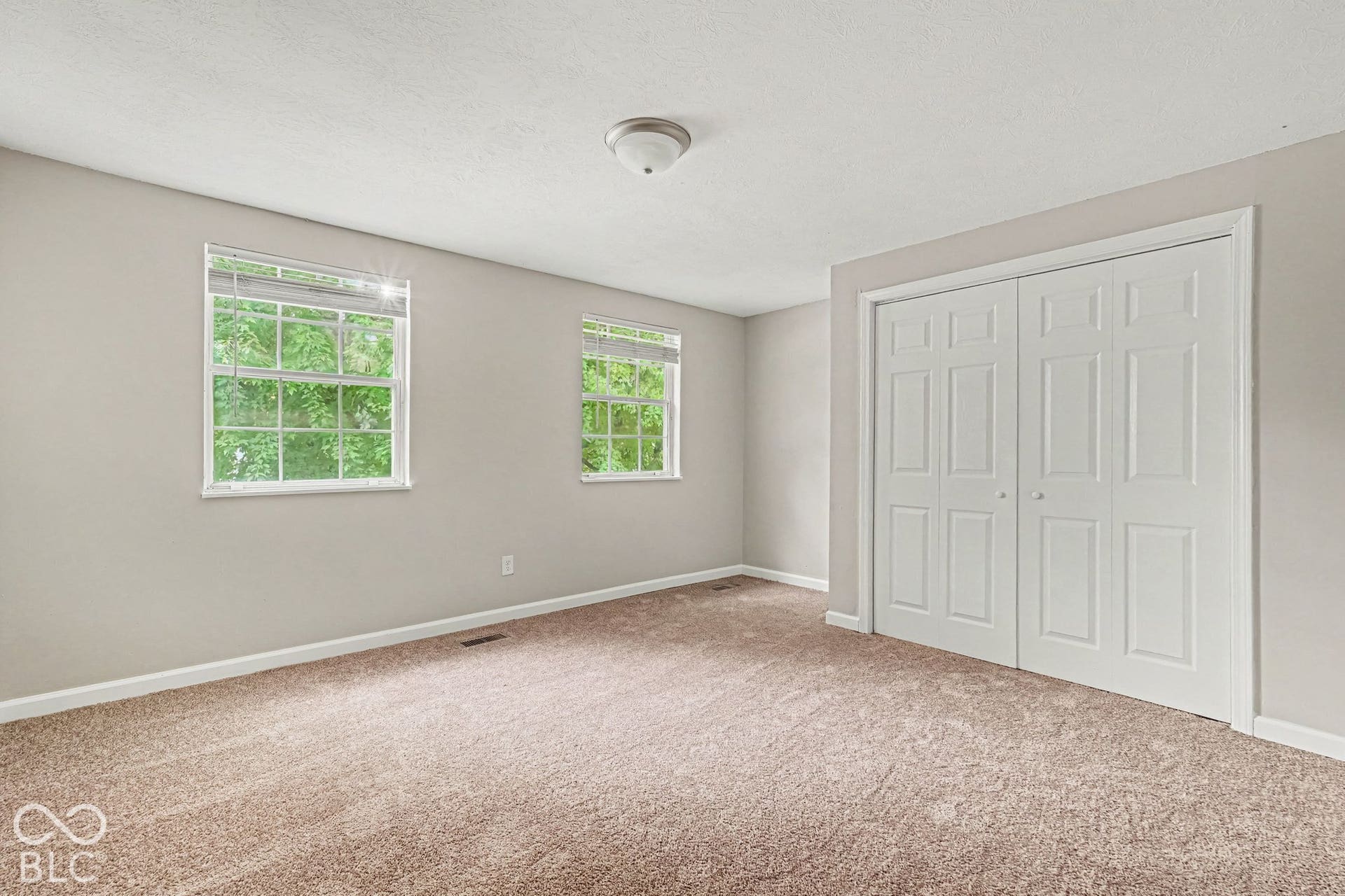 Soft neutral carpet flooring, two sash windows with blinds, a ceiling-mounted light fixture, and white bi-fold closet doors