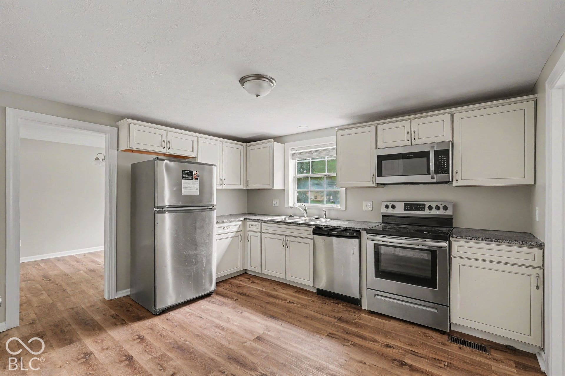 Wood-finish flooring, white cabinetry, stainless steel appliances, dark countertops, and a single basin sink
