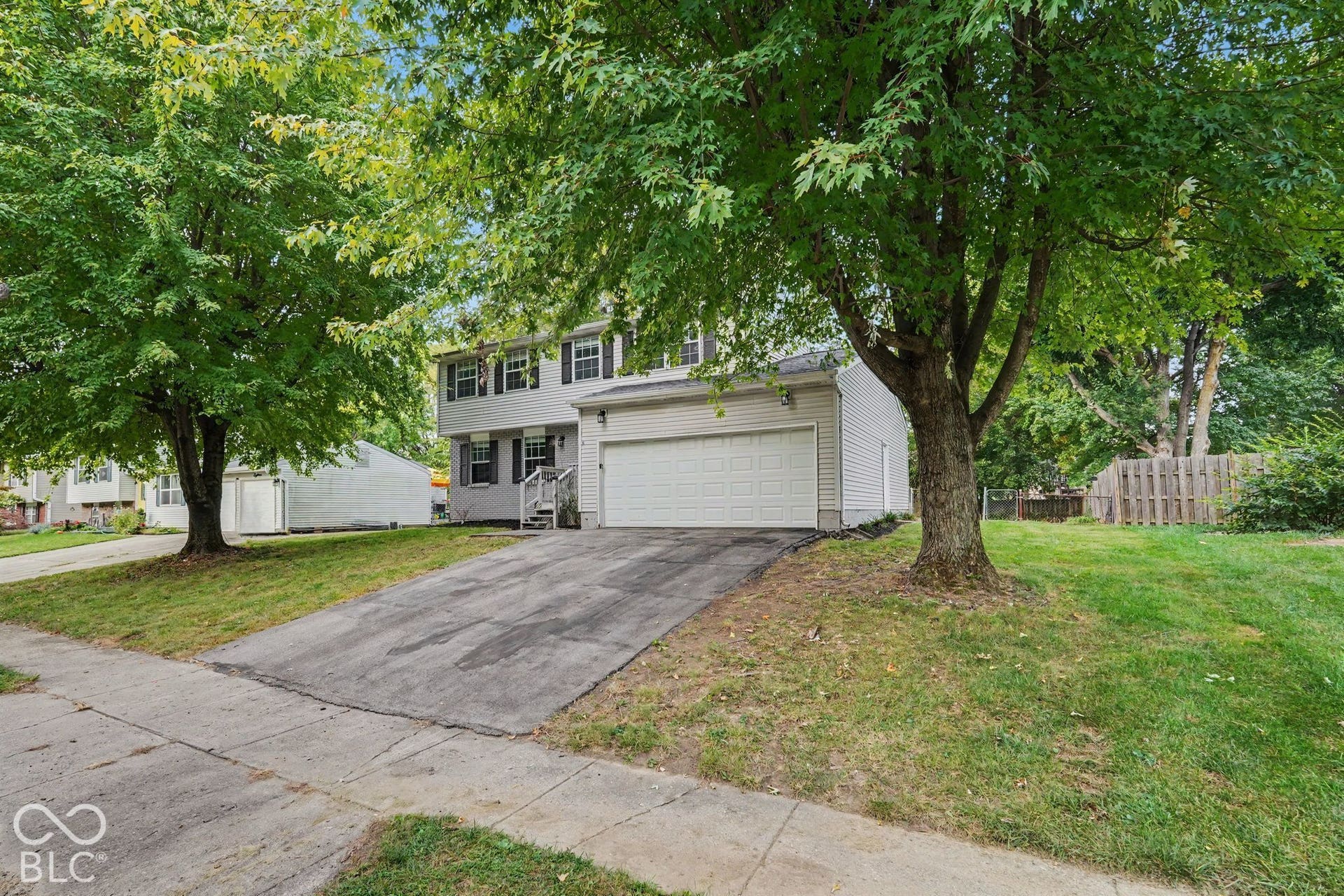 Two-story residence with a two-car garage, mature trees, and a concrete driveway