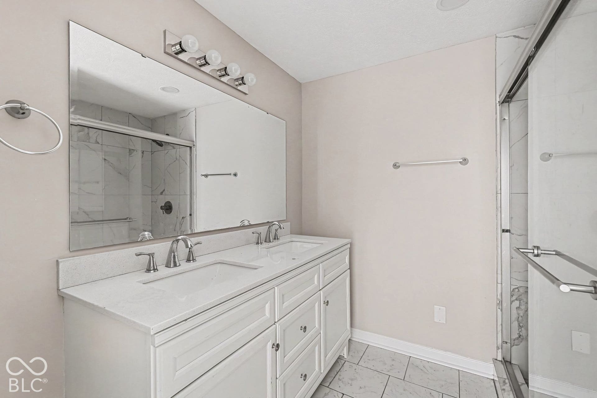 Dual vanity with white cabinetry and integrated sinks, wide wall-mounted mirror, contemporary light fixture, and glass-enclosed shower with tile surround
