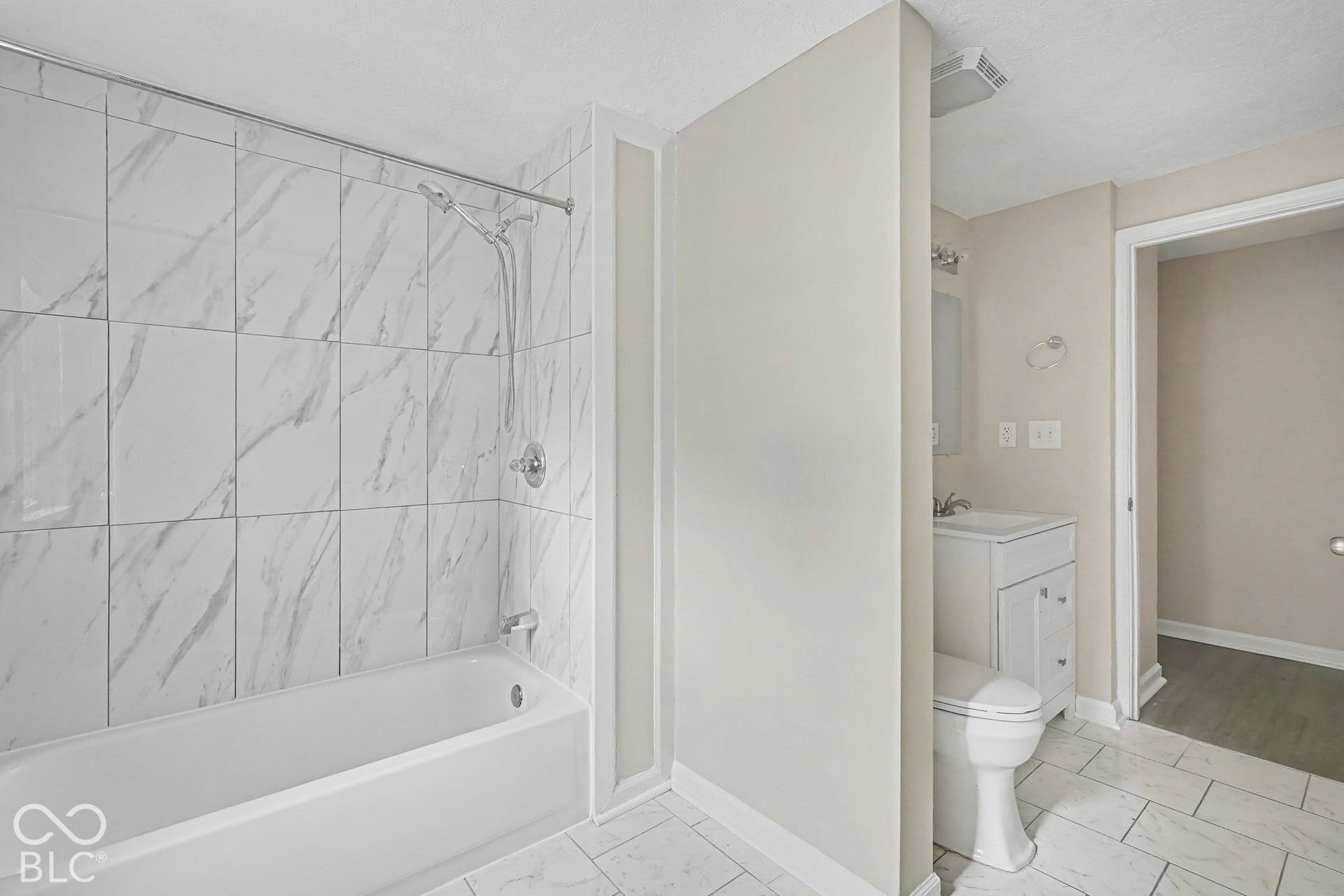 Bathtub with white subway tile surround, chrome shower fixture, single vanity with integrated sink, and white tile flooring