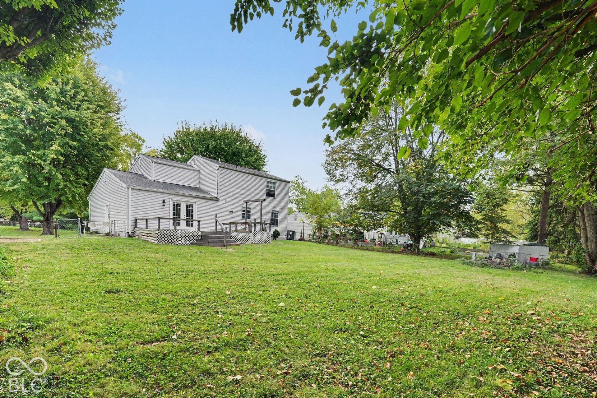 Expansive green lawn with mature trees and a multi-level deck featuring white lattice skirting