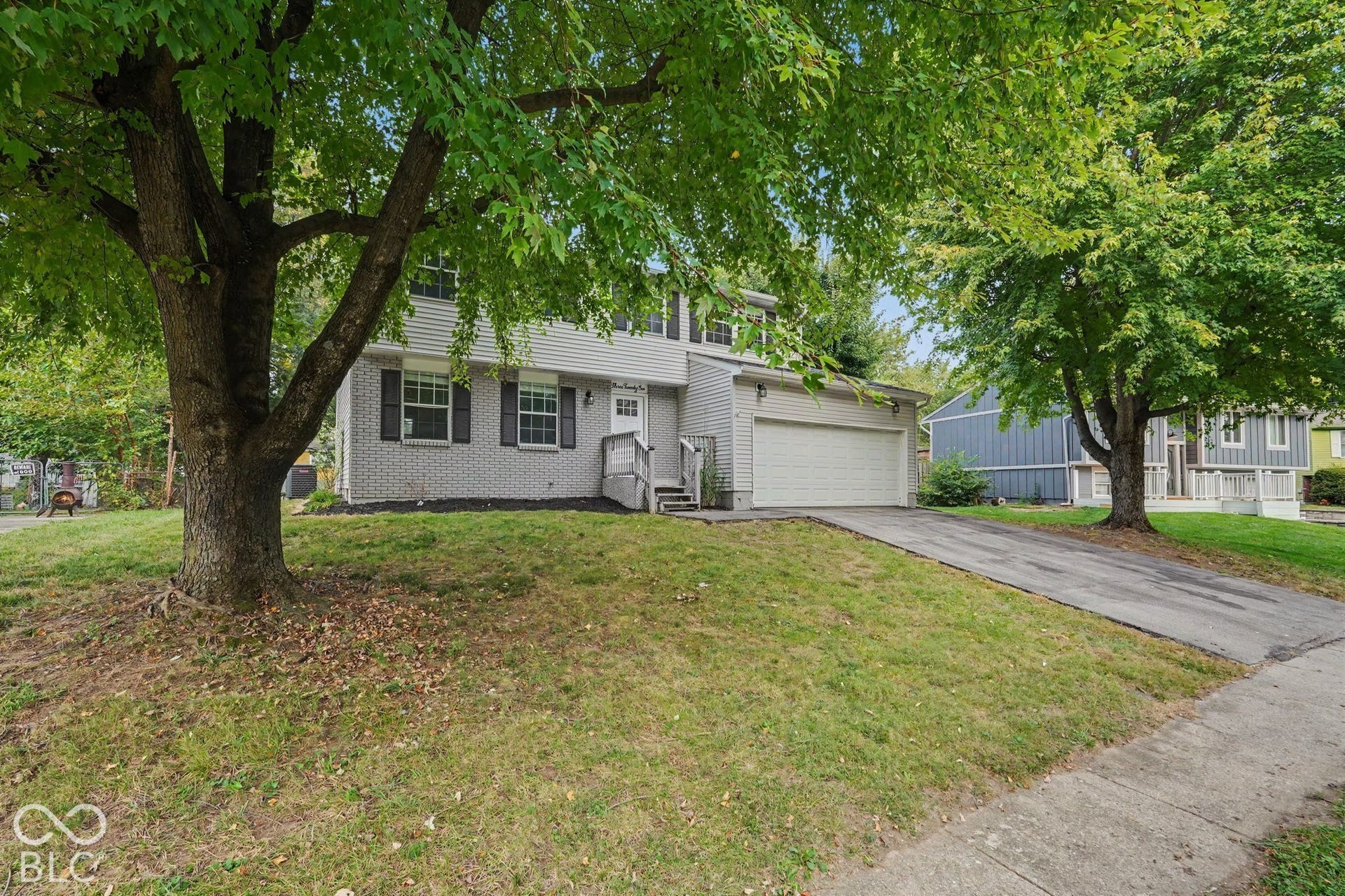 Two-story residence featuring light gray siding, a white garage door, a front entry with steps, and a paved driveway
