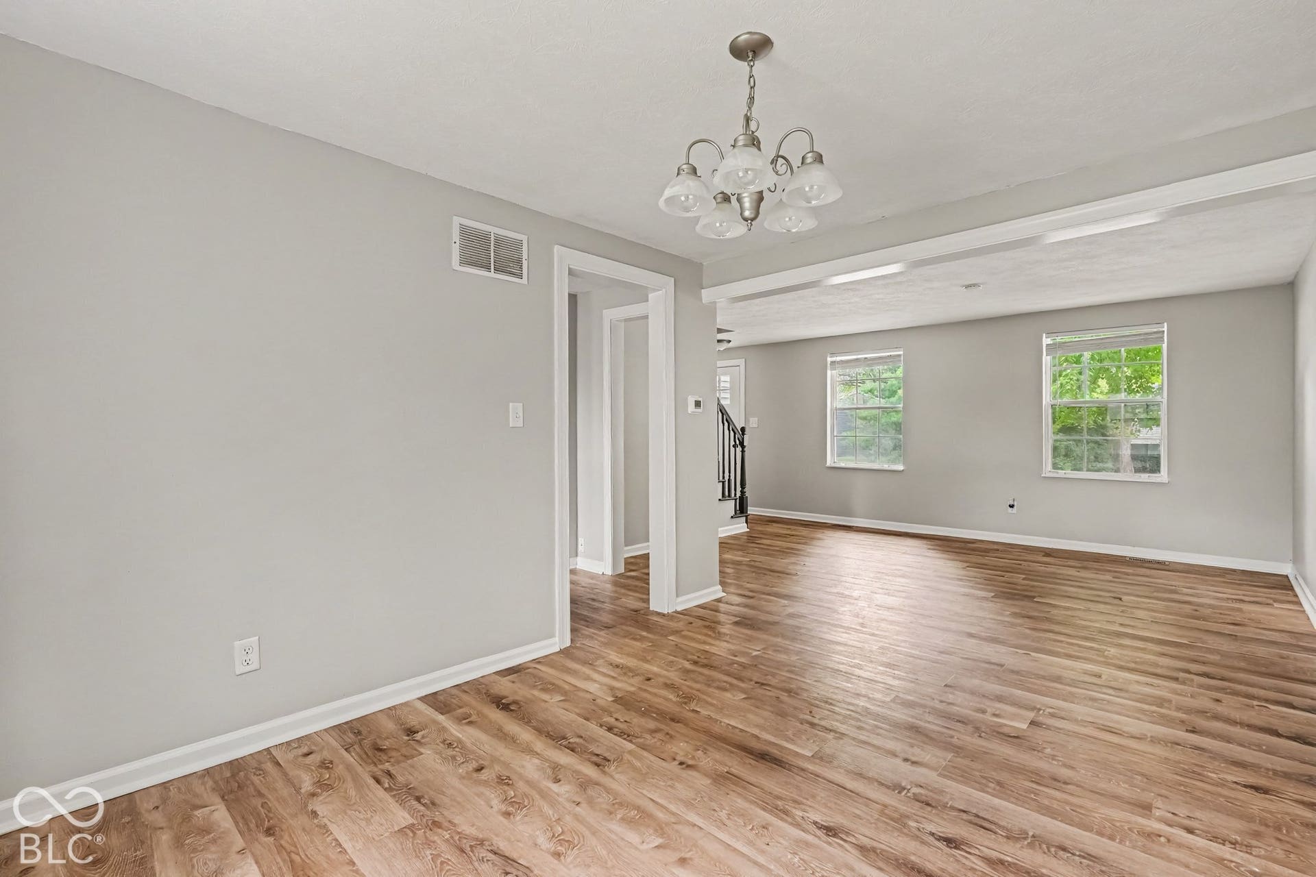 Wood-finish flooring, light gray wall paint, white trim, two windows, and a chandelier with frosted glass shades