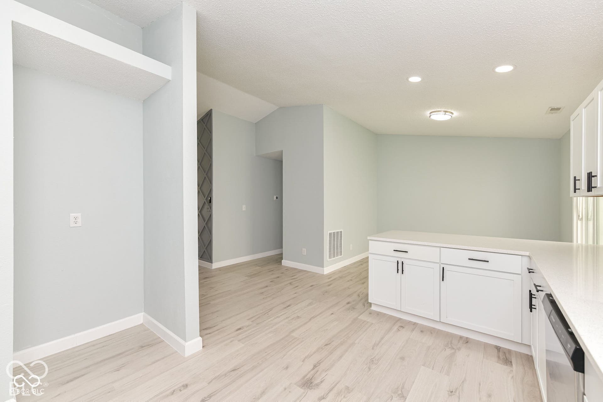 Open-concept interior featuring light wood-finish flooring, white cabinetry with matte black hardware, and light-toned walls