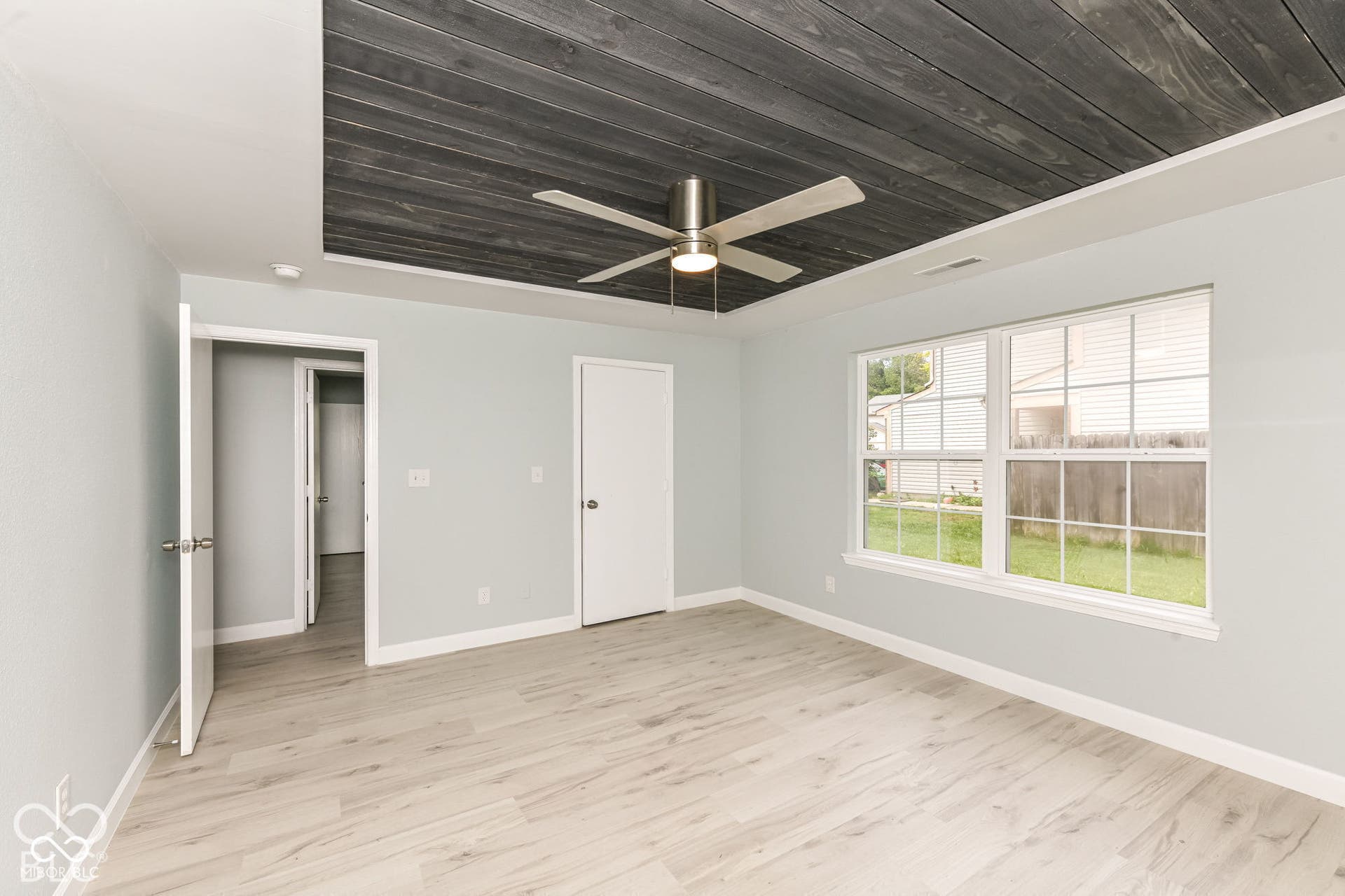 Recessed wood-panel ceiling with a ceiling fan, light wood-finish flooring, and a large window