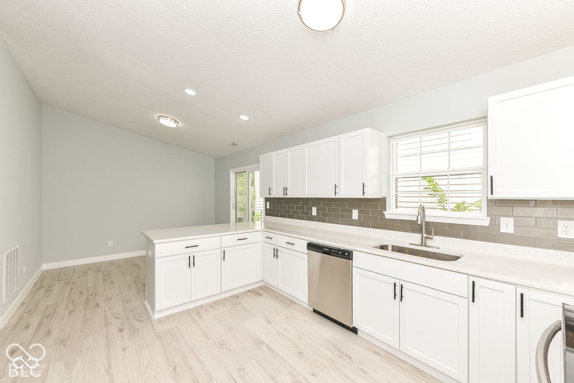 Kitchen featuring white cabinetry, light-toned wood-finish flooring, stainless steel dishwasher, white countertops, and a gray subway tile backsplash