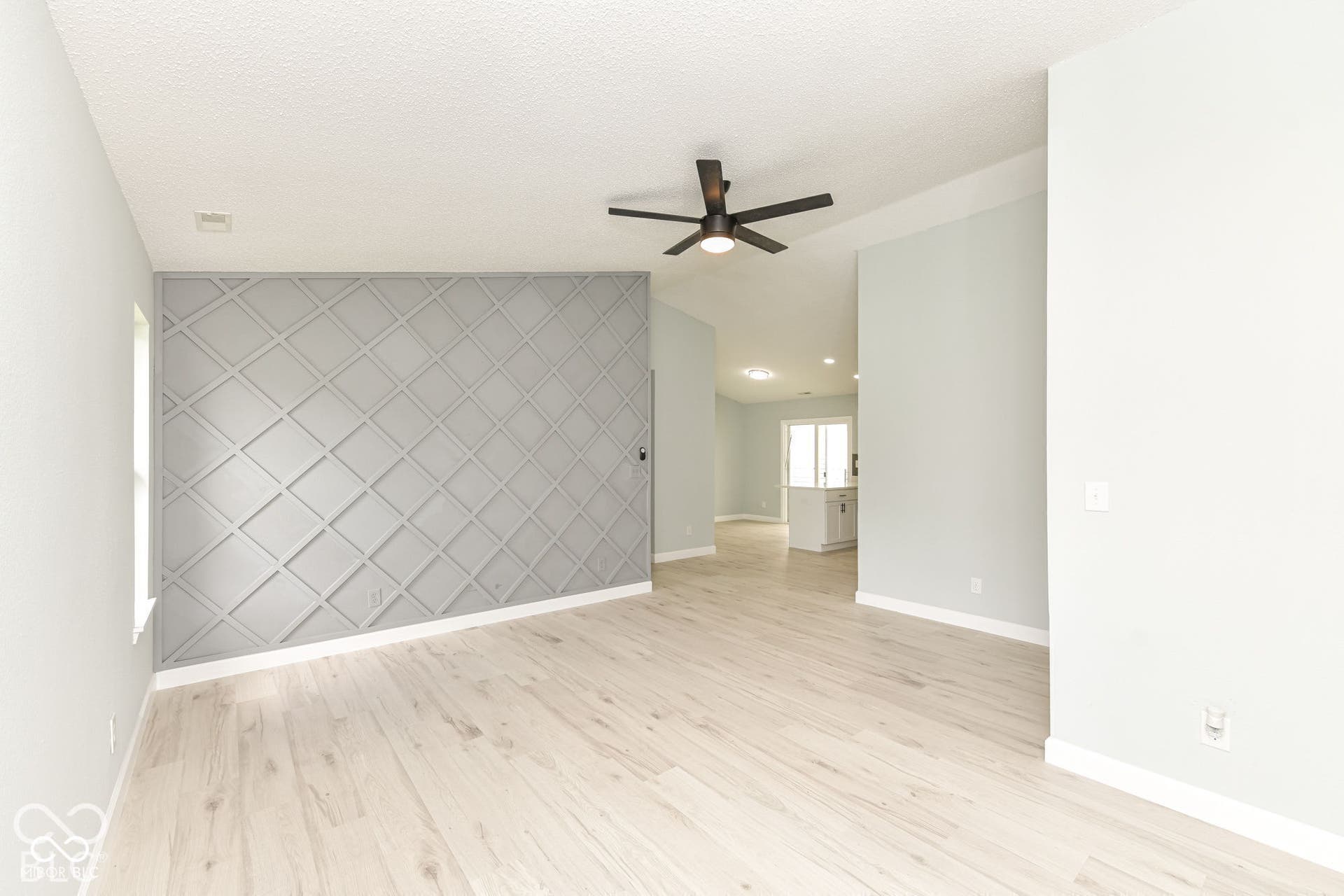 Light-toned wood-finish flooring, vaulted ceiling, contemporary ceiling fan, and an accent wall featuring a geometric lattice design