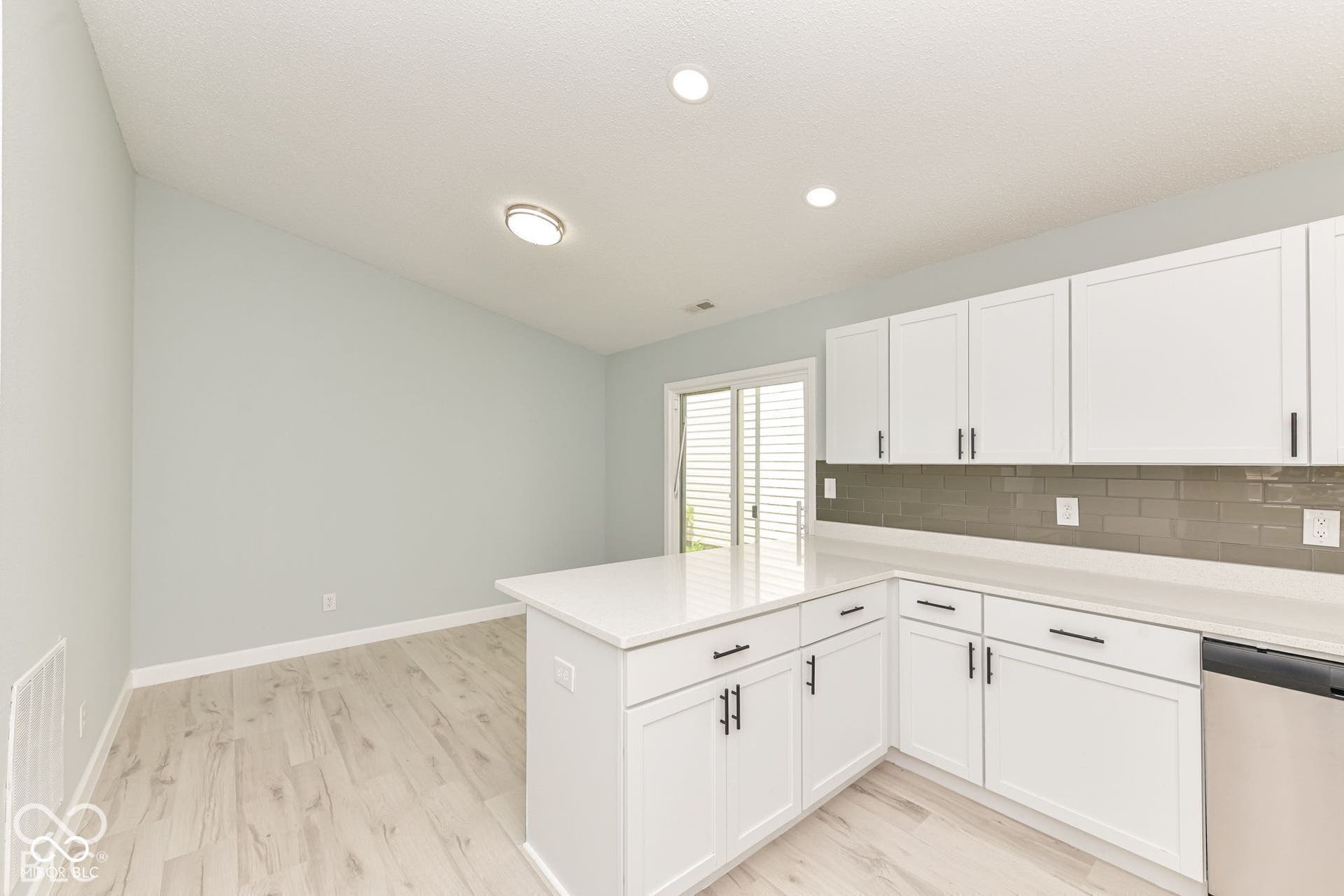 White shaker cabinetry with dark hardware, light countertops, subway tile backsplash, stainless steel dishwasher, and wood-finish flooring