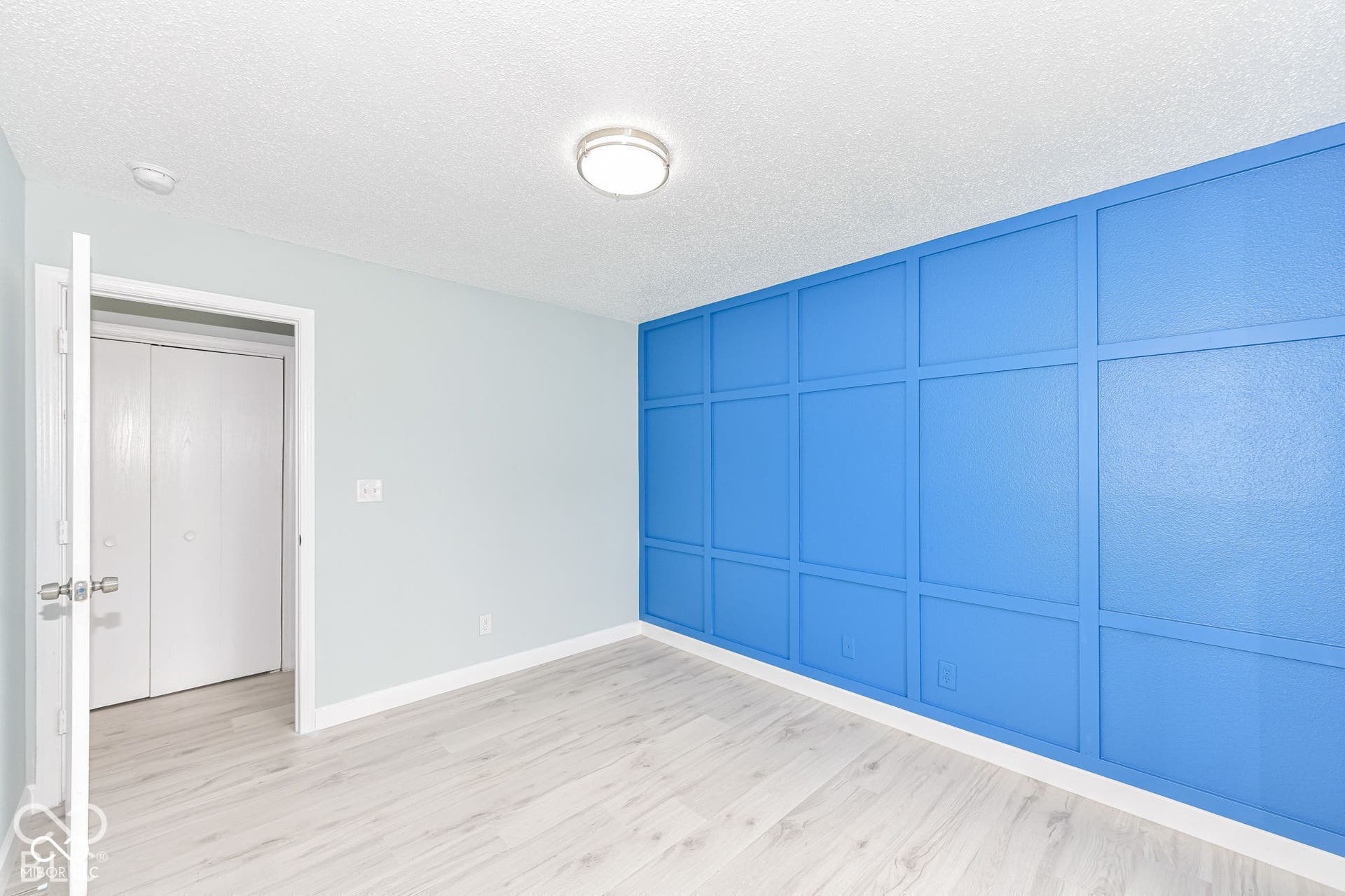 Wood-finish flooring with white baseboards, a blue accent wall with decorative paneling, light blue painted walls, and a flush mount ceiling light