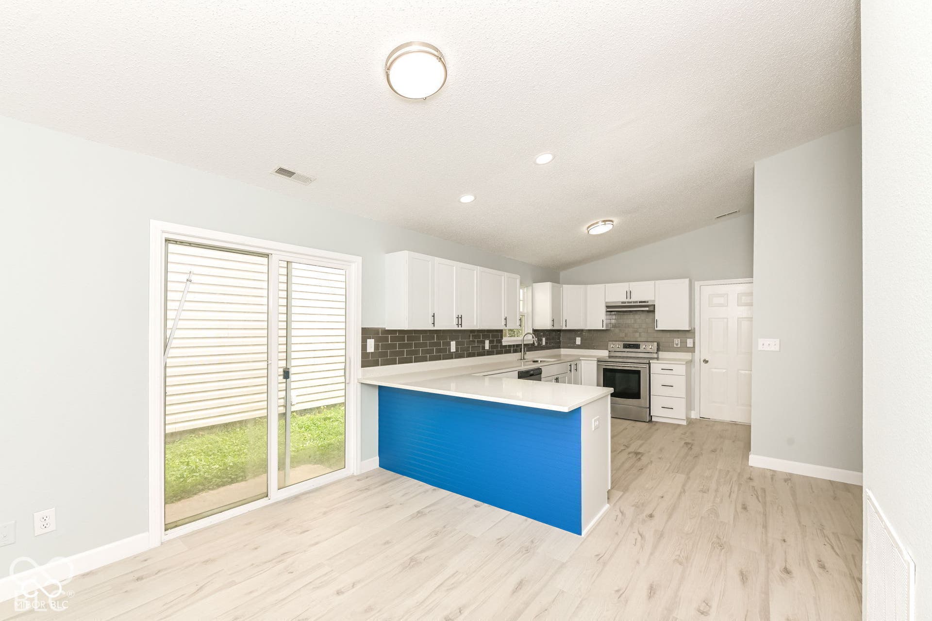 Vaulted ceiling, wood-finish flooring, white cabinetry, stainless steel appliances, and a sliding glass door