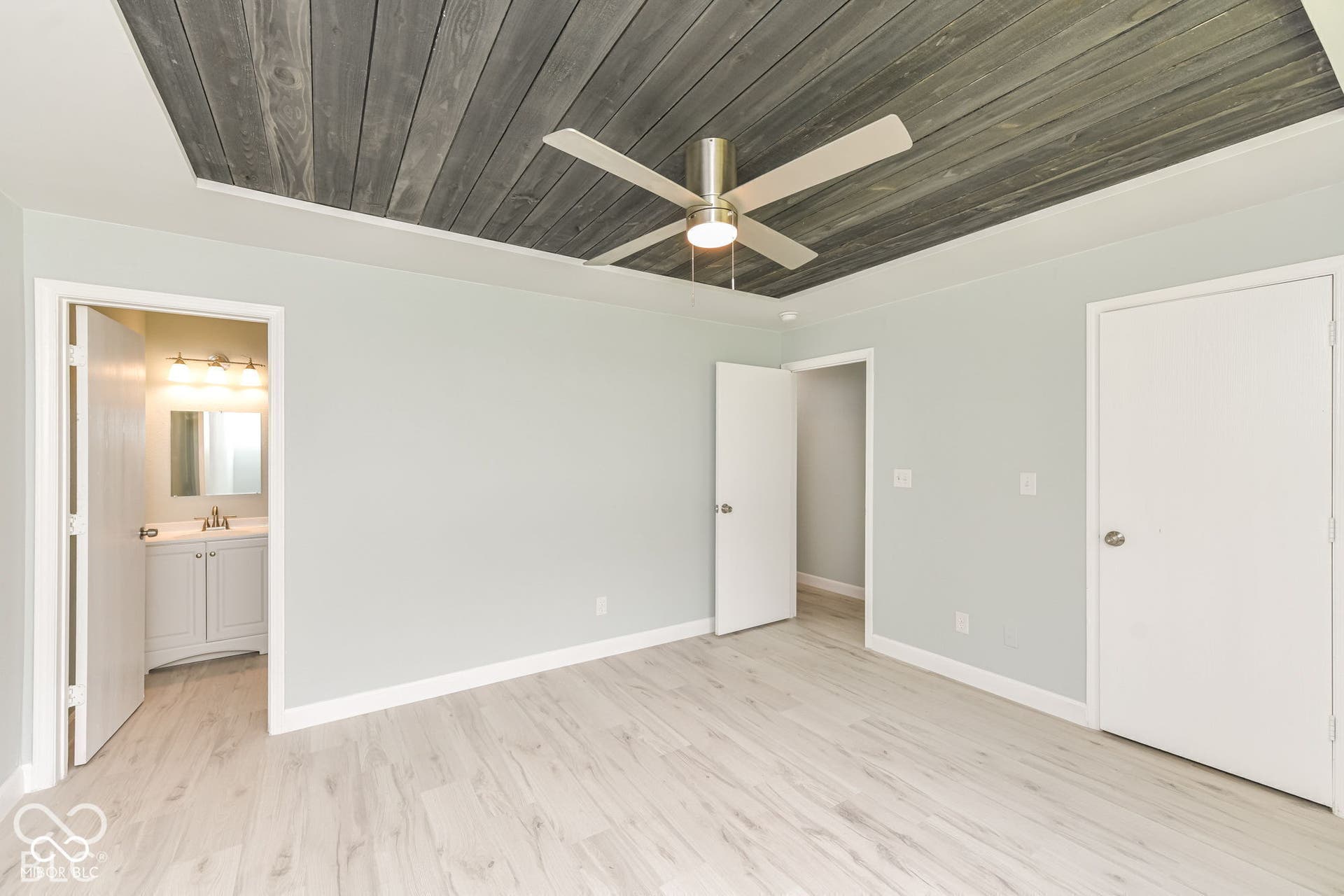 Tray ceiling with wood-finish paneling, contemporary ceiling fan, and wood-finish flooring
