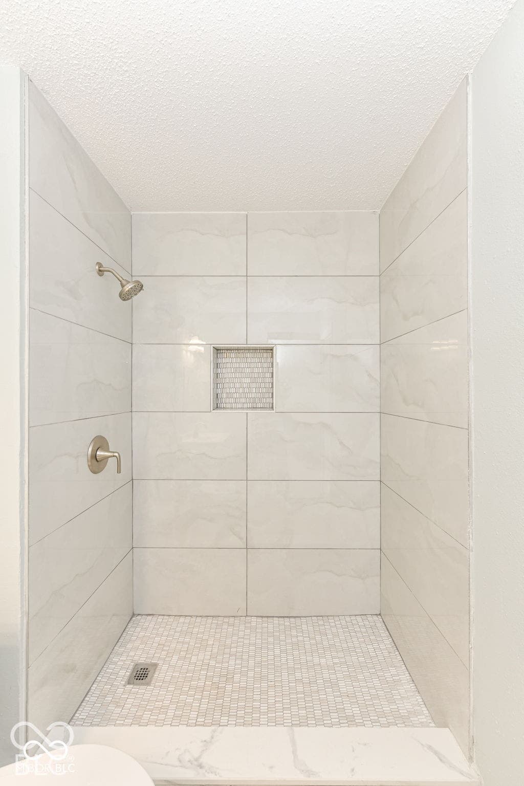 Tiled shower with a niche, featuring a tile mosaic floor and brushed nickel fixtures