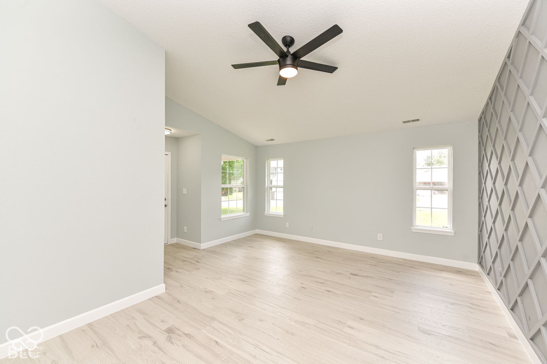 Vaulted ceiling, wood-finish flooring, black ceiling fan, decorative wall paneling, and multiple windows