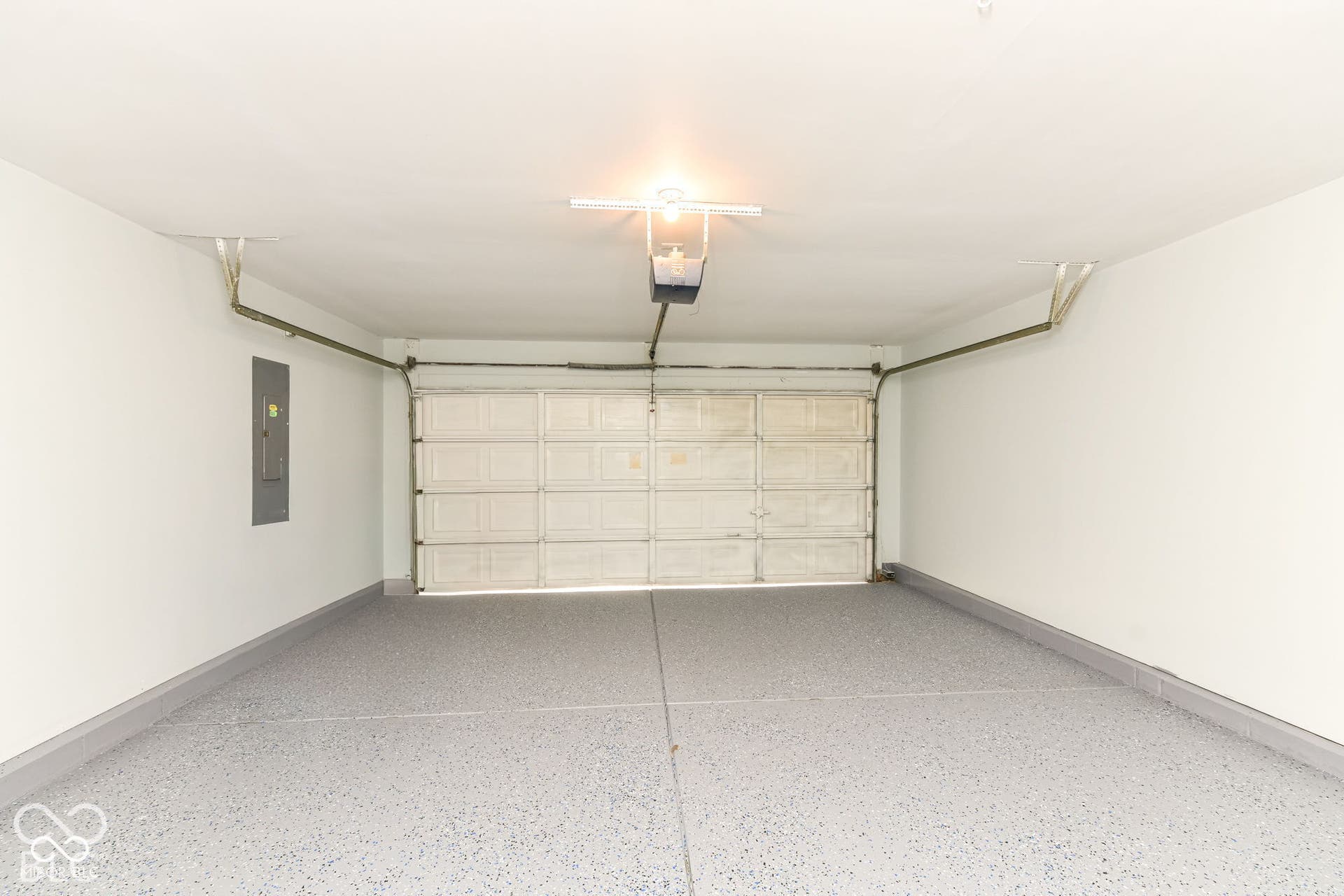 Attached two-car garage featuring a light-toned speckled epoxy floor, white walls, and an overhead garage door opener