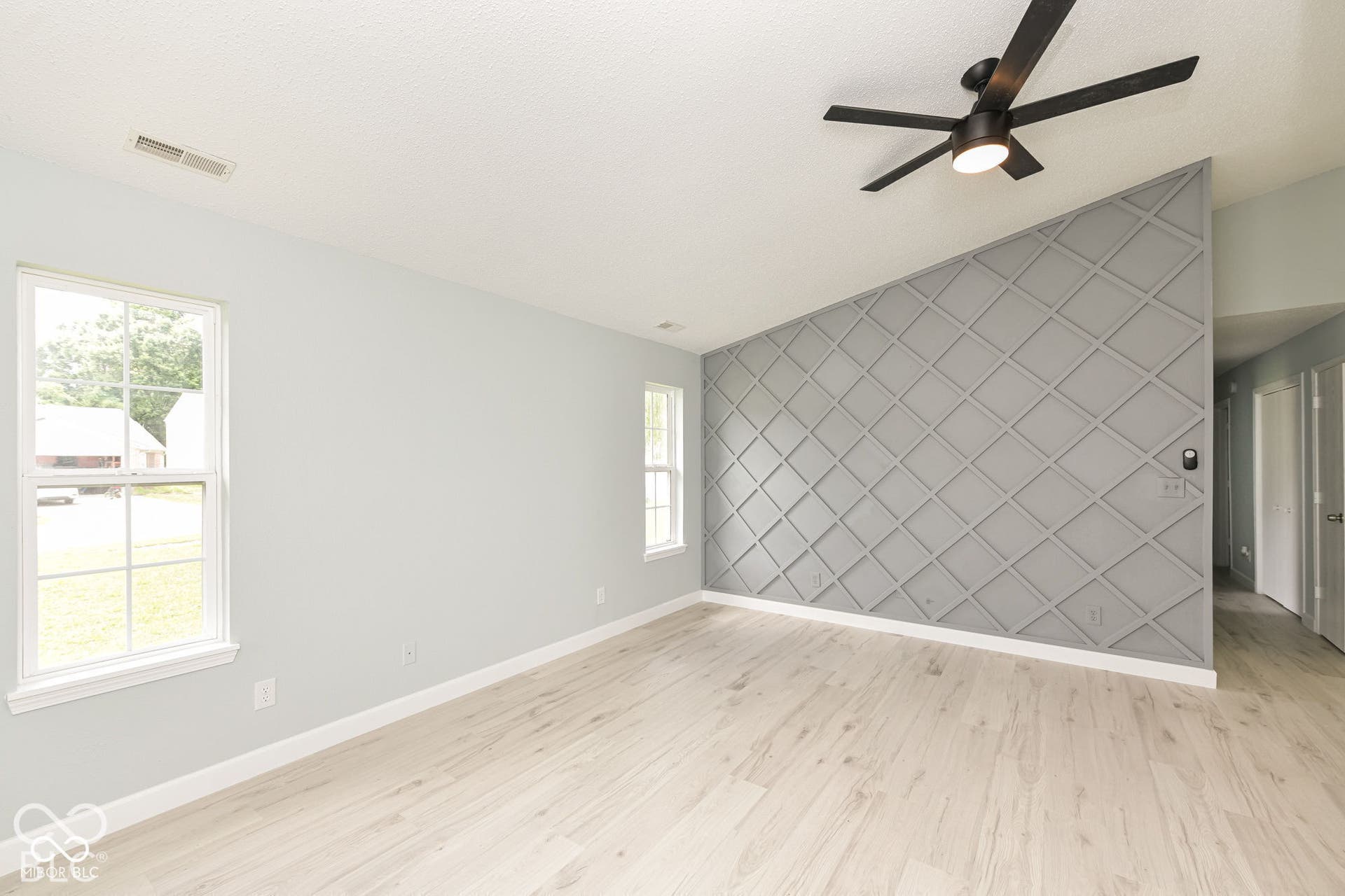 Vaulted ceiling featuring a black ceiling fan, accent wall with geometric molding, light wood-finish flooring, and white trim windows