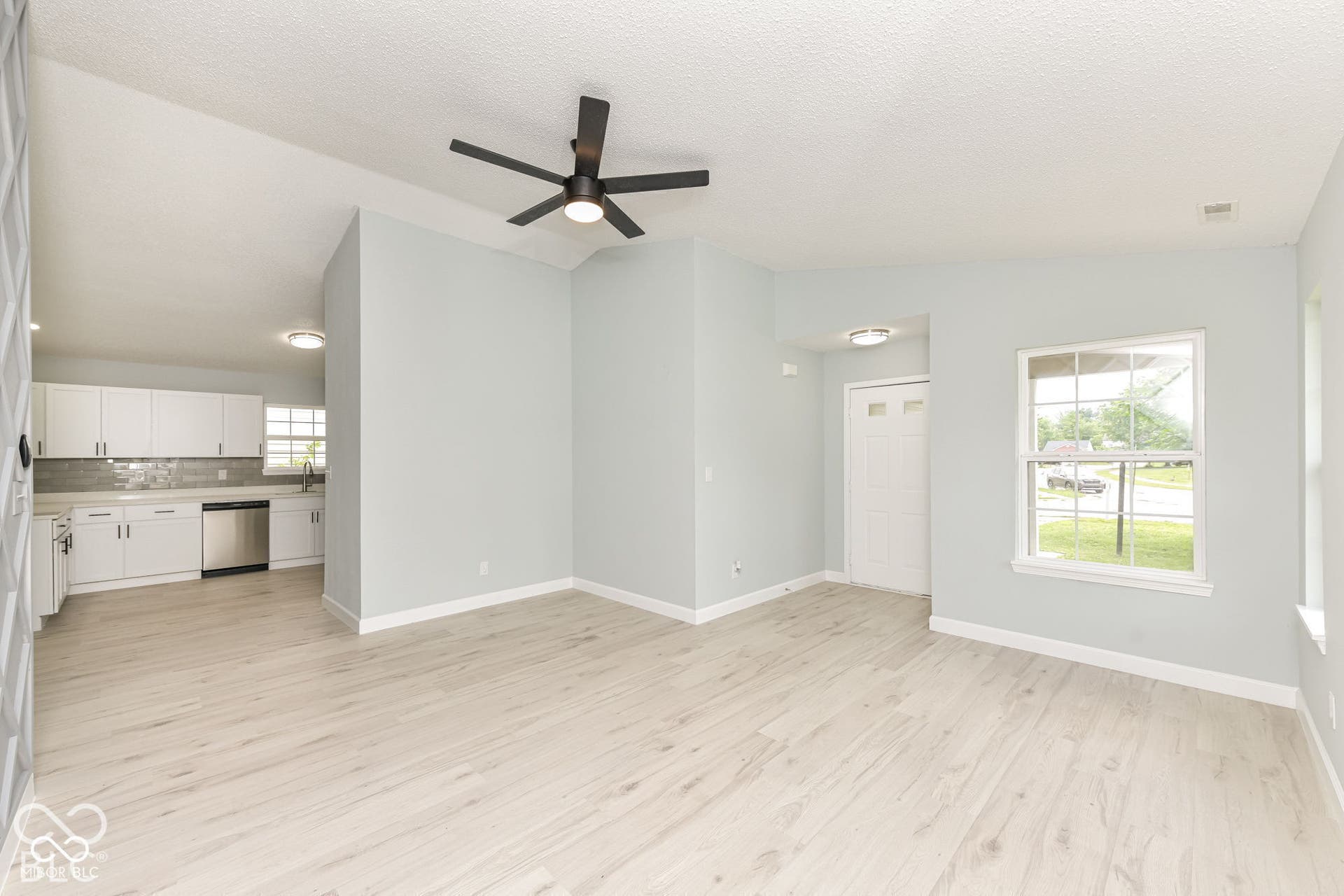 Vaulted ceiling, wood-finish flooring, a contemporary ceiling fan, and a kitchen featuring white cabinetry with stainless steel appliances