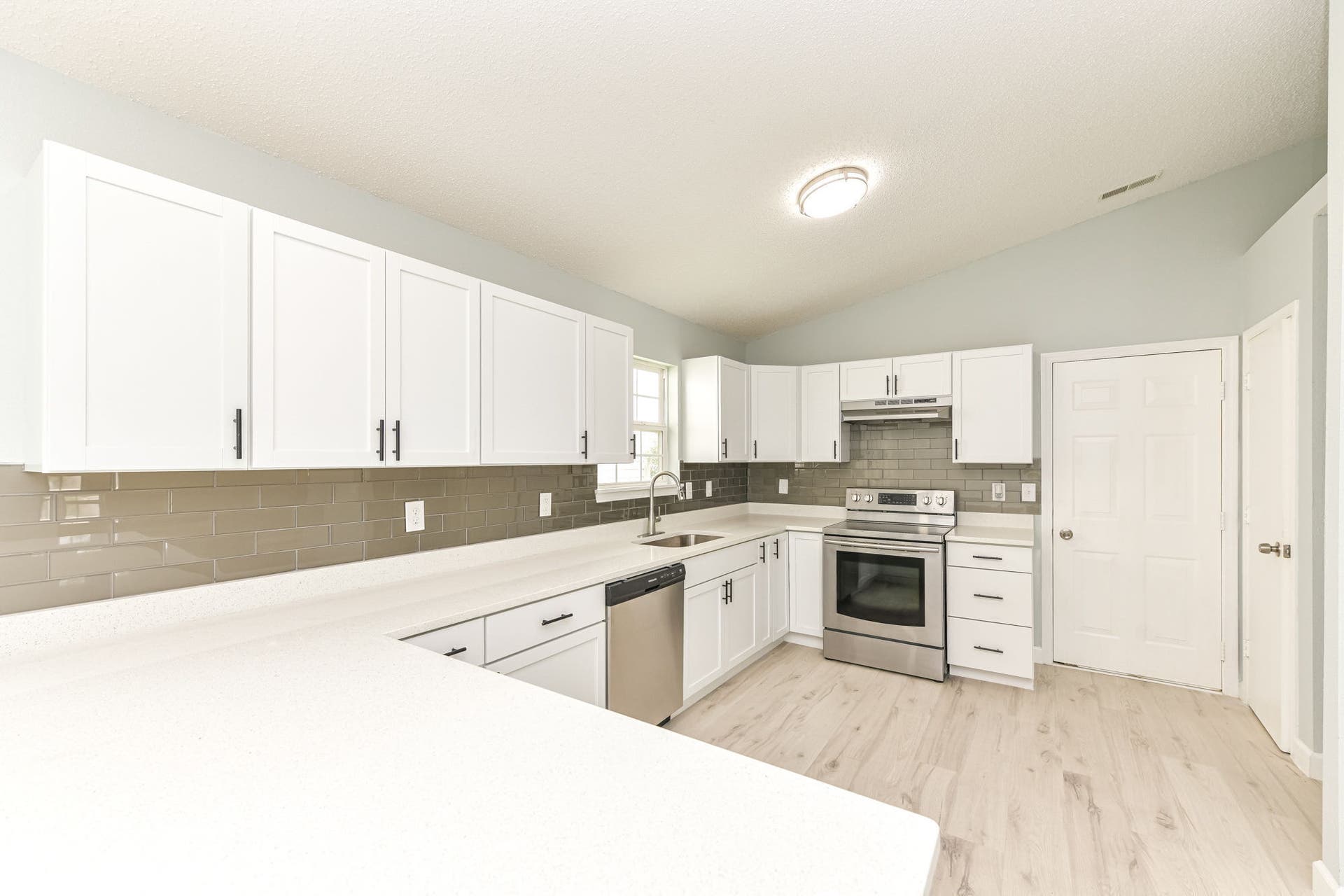 Contemporary kitchen featuring white cabinetry, light countertops, stainless steel appliances, a subway tile backsplash, and light wood-finish flooring