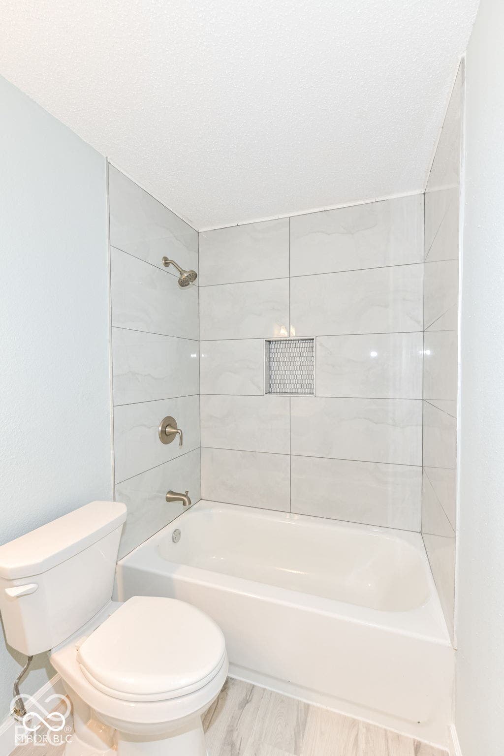 Bathtub with subway tile surround, integrated shower niche with mosaic tile, brushed nickel fixtures, and wood-finish flooring
