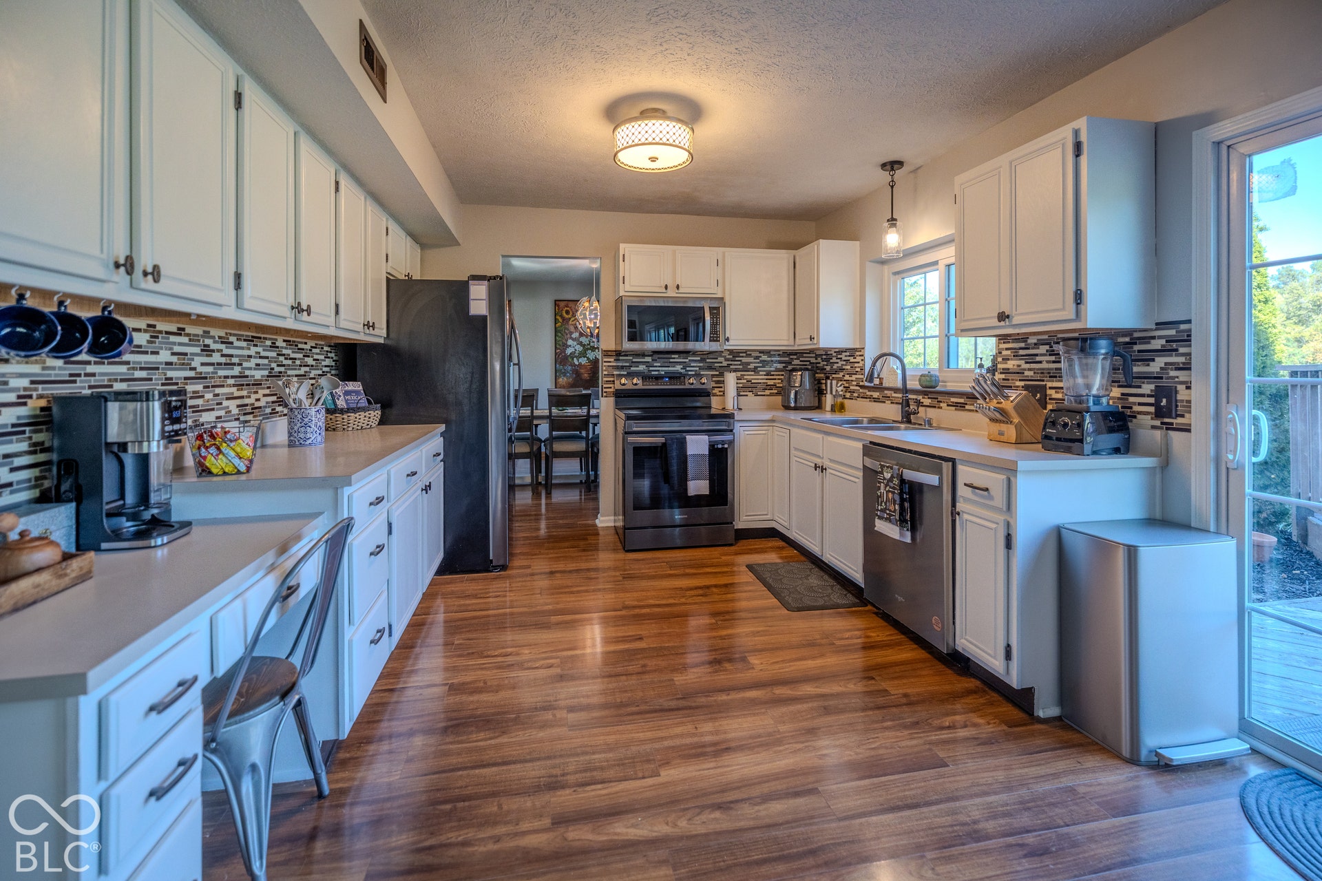 6416 Manchester Drive, Fishers, IN 46038 Chef's kitchen featuring white cabinetry, stainless steel appliances, wood-finish flooring, mosaic tile backsplash, and abundant countertops.