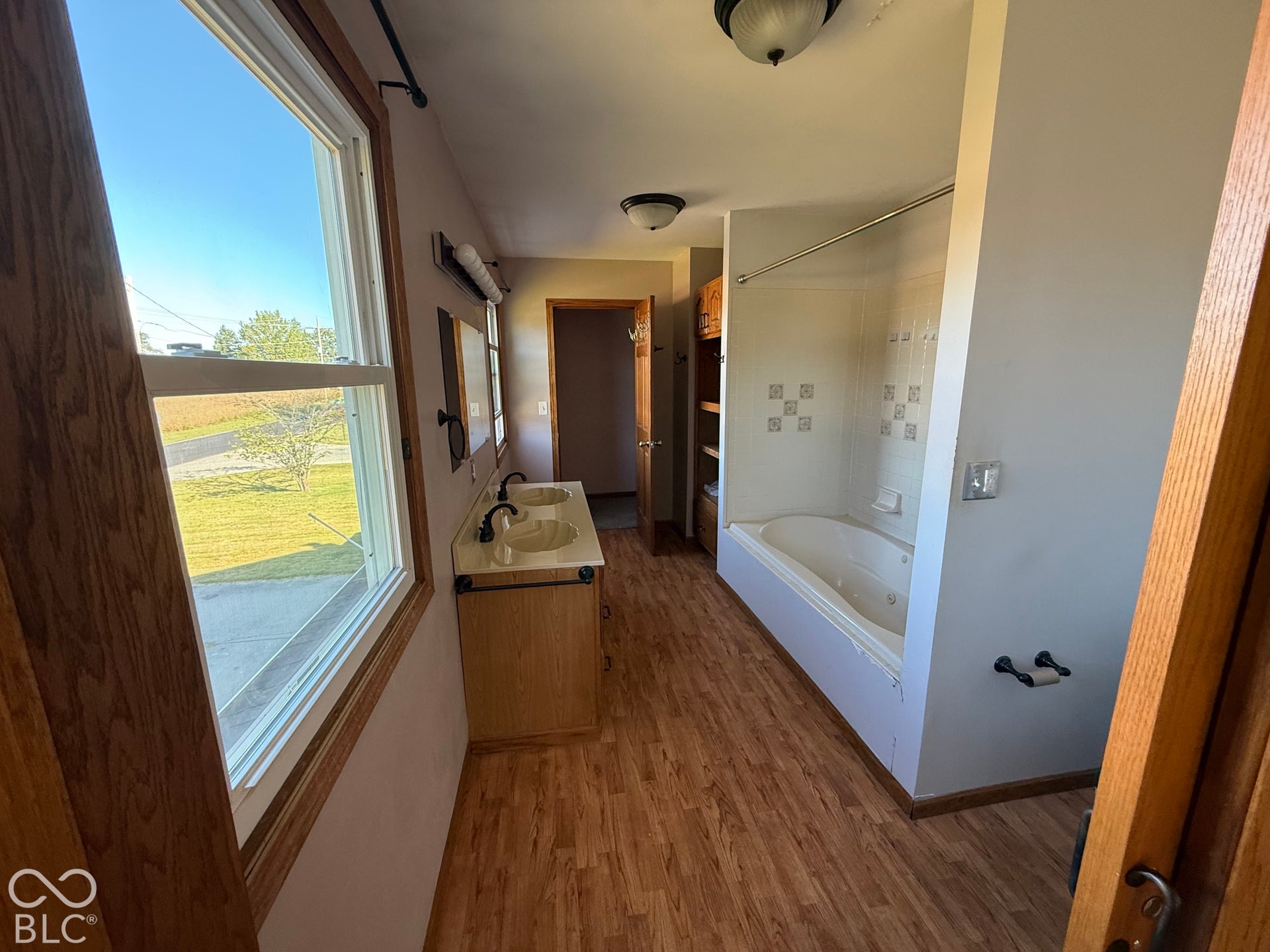 Double vanity with integrated sinks, jetted bathtub, wood-finish flooring, and white-framed window