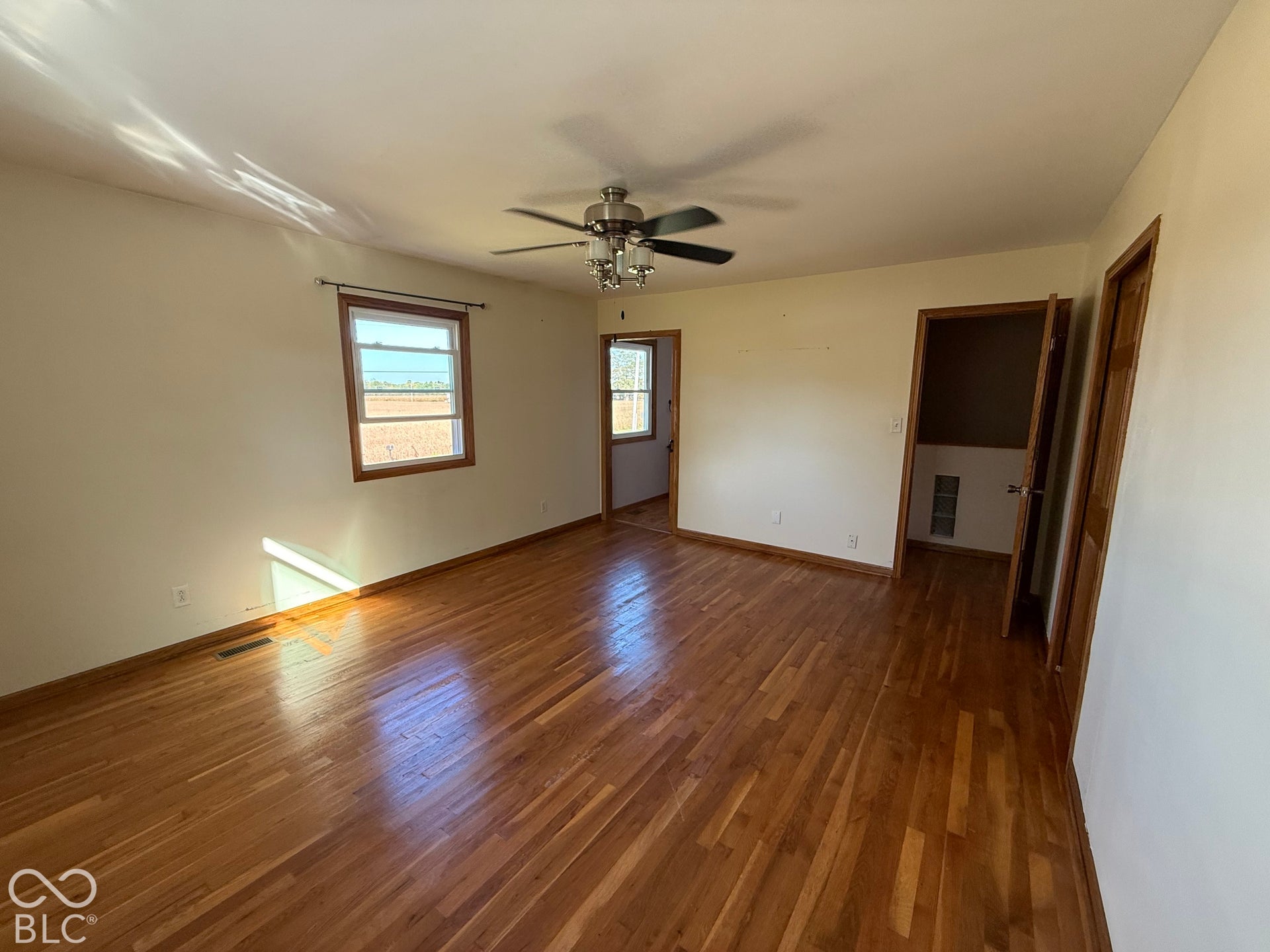 Hardwood flooring, two windows with wood trim, ceiling fan light fixture, and a closet with wood trim