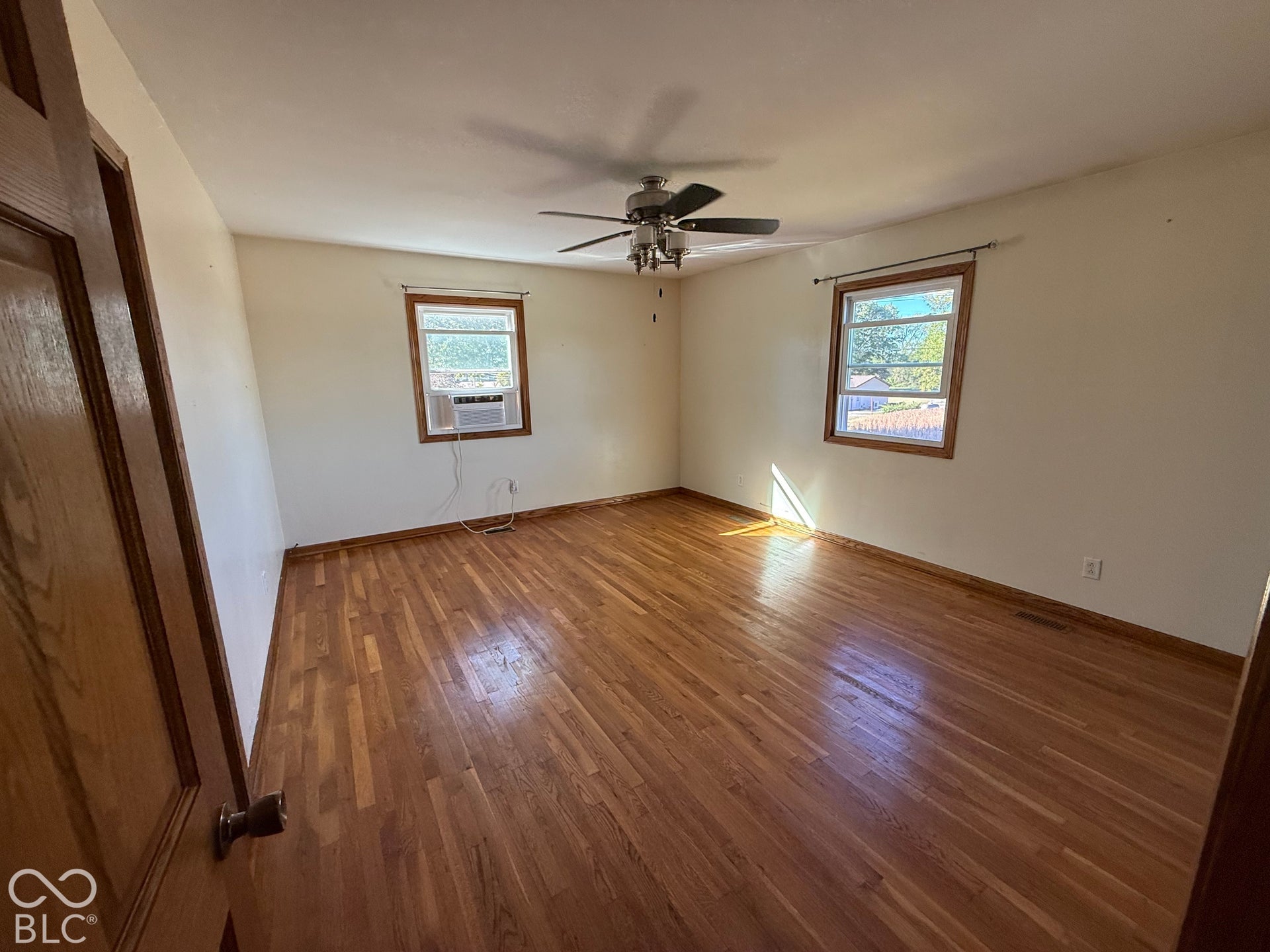 Hardwood flooring, ceiling fan with integrated lighting, wood-framed windows, and a wood panel door
