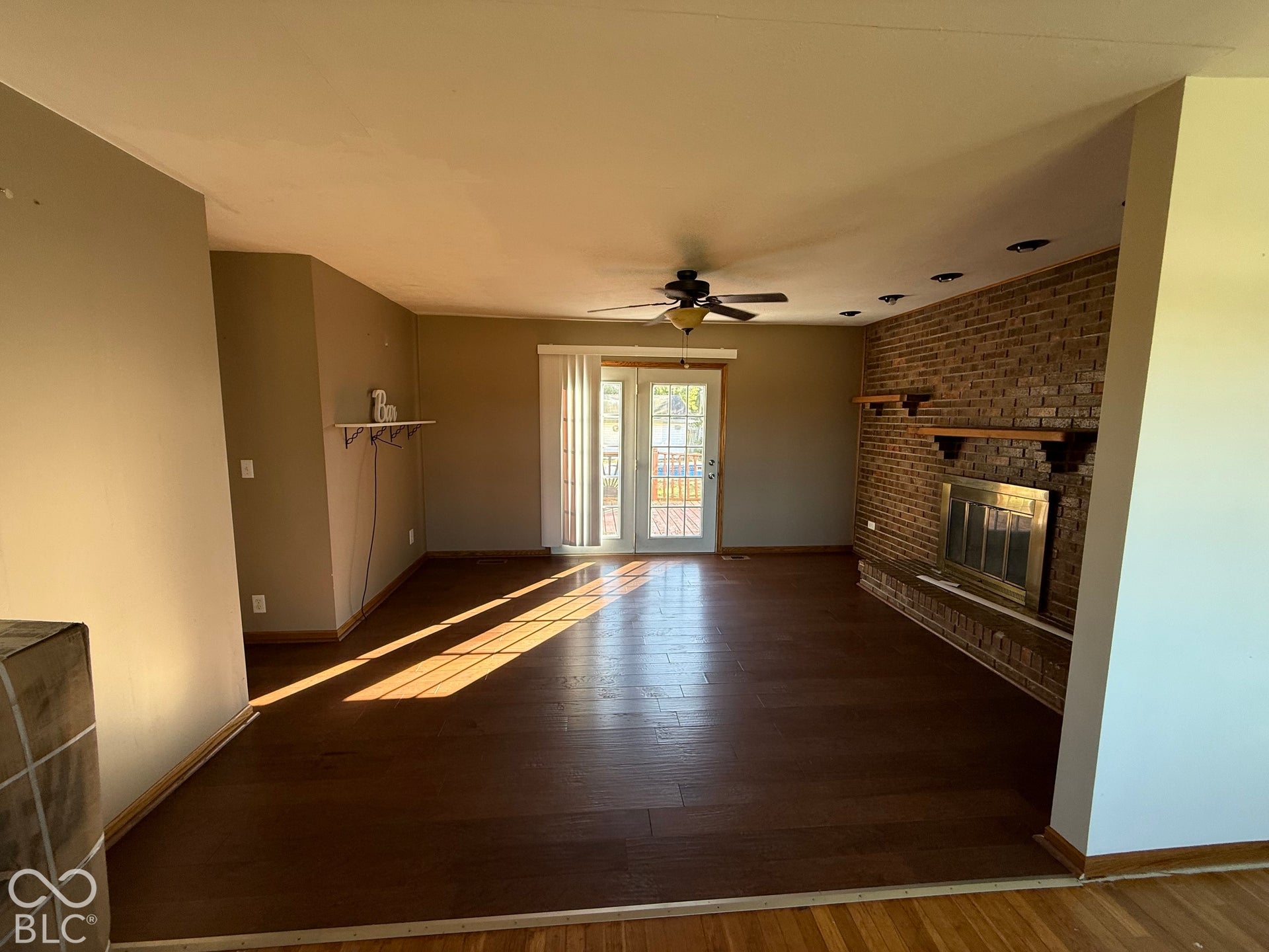 Brick accent wall with fireplace, recessed ceiling lighting, wood-finish flooring, ceiling fan, and sliding glass door with integrated blinds