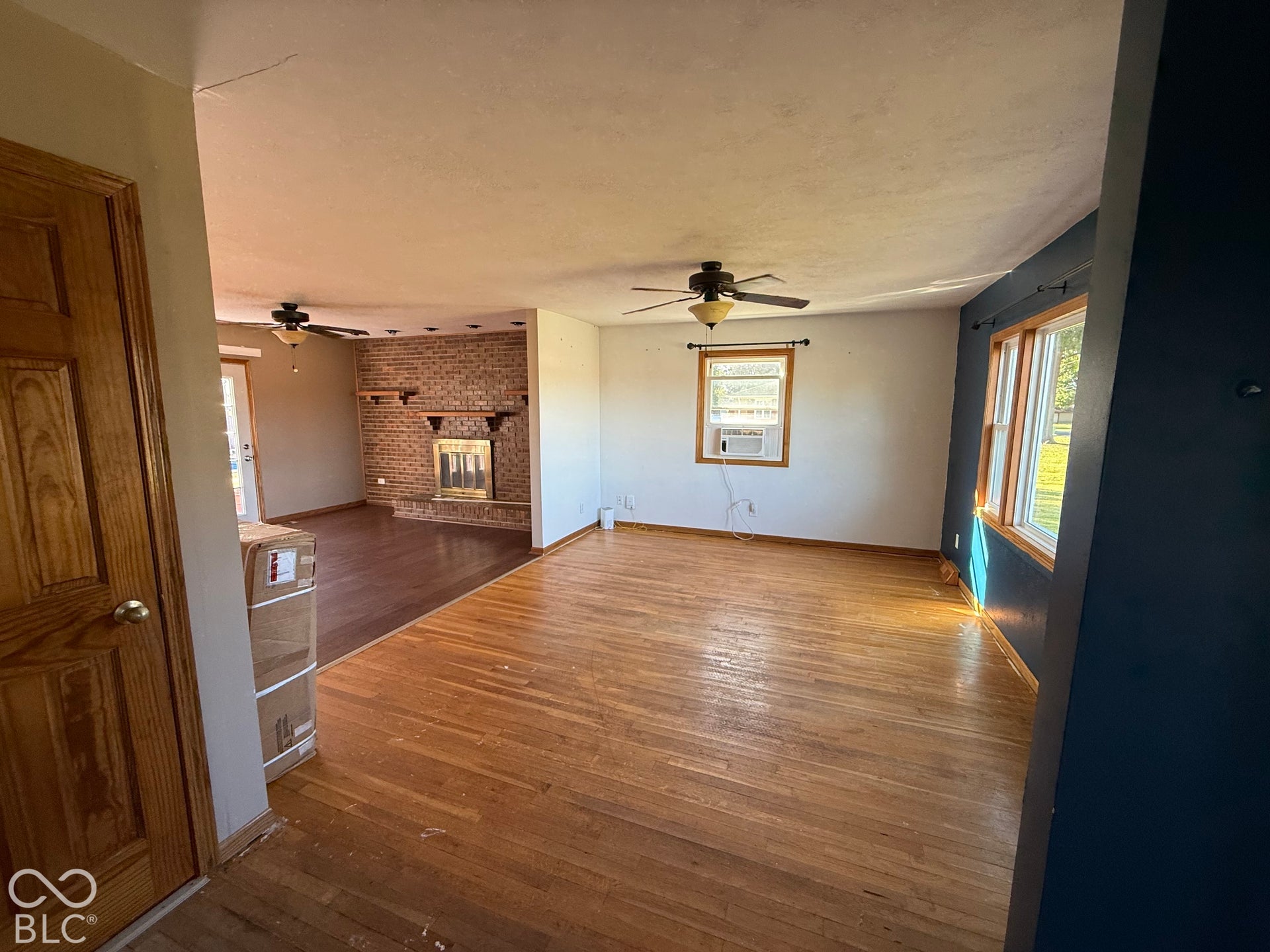 Hardwood flooring, brick fireplace with mantel, ceiling fans, and multiple windows