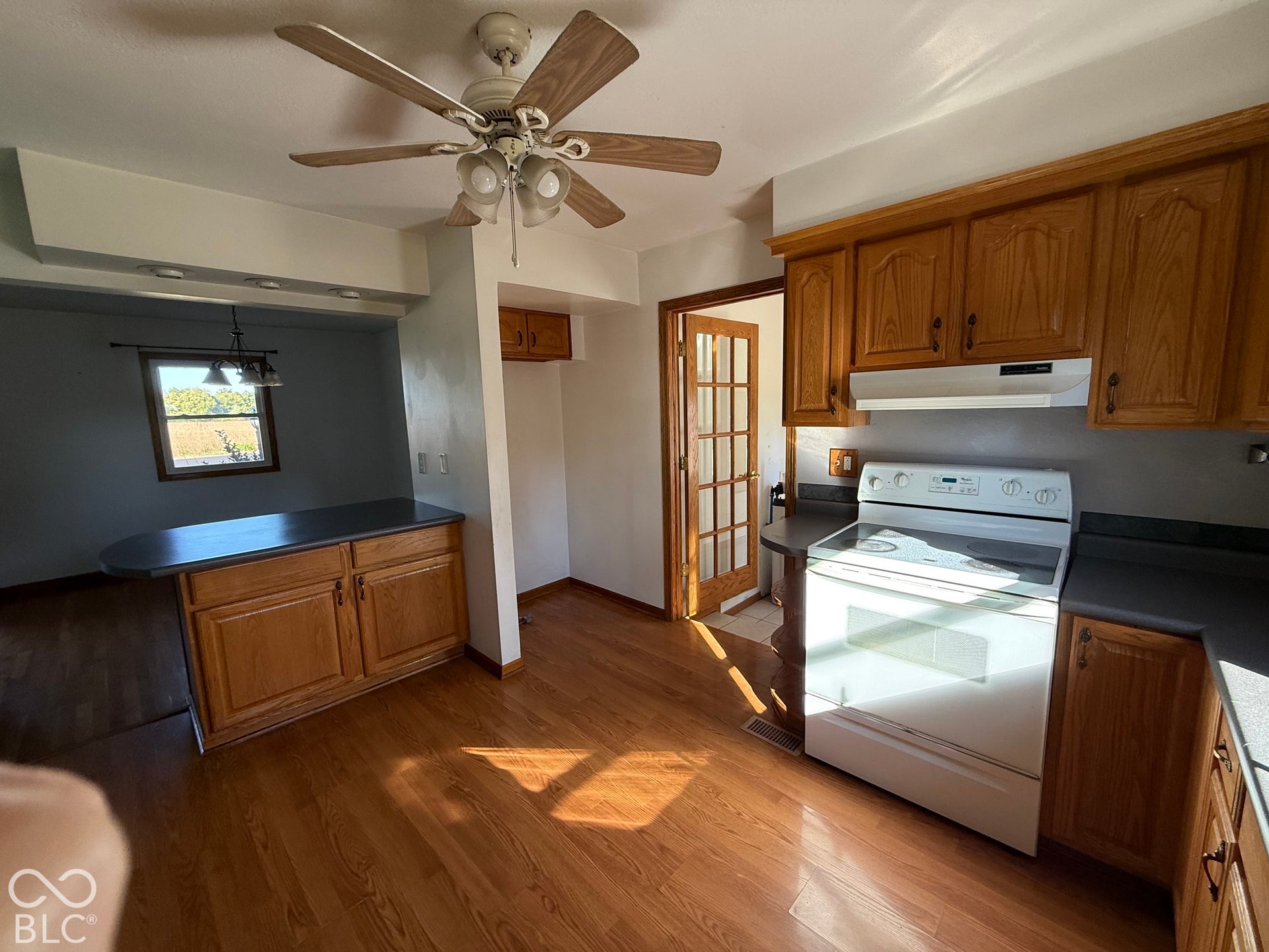 Wood-finish flooring, wood cabinetry, built-in electric range, ceiling fan with light, and a french door