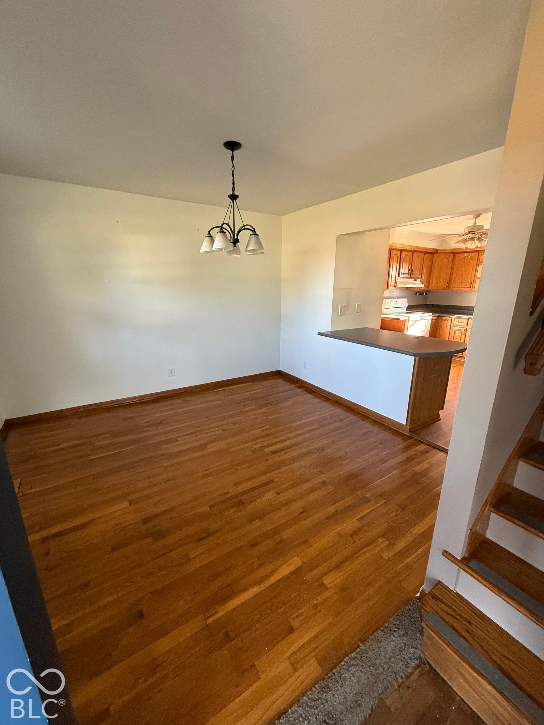 Hardwood flooring throughout, contemporary chandelier, breakfast bar, and staircase with wood treads