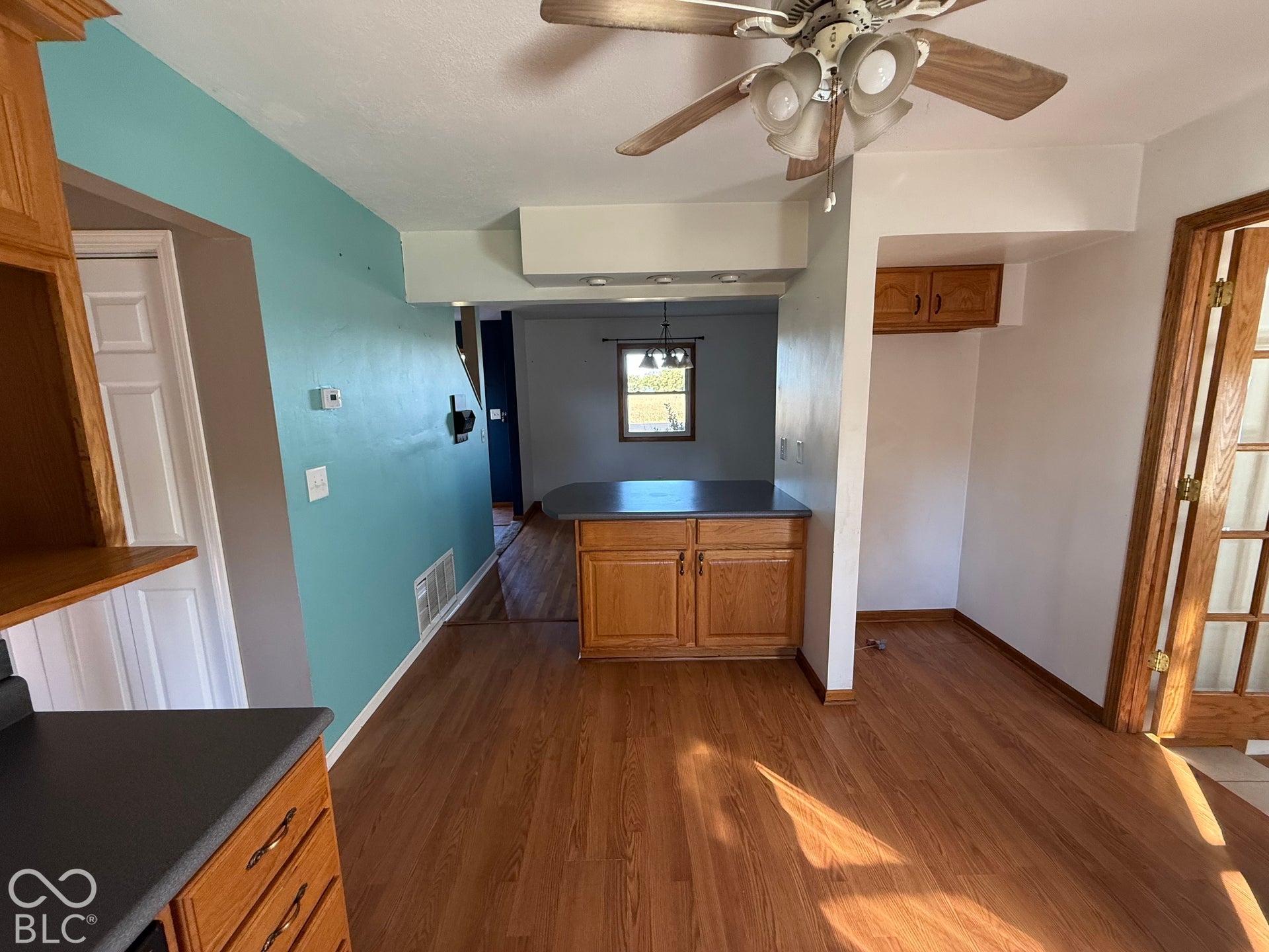 Wood-finish flooring, ceiling fan with light fixture, built-in cabinetry, and a countertop island