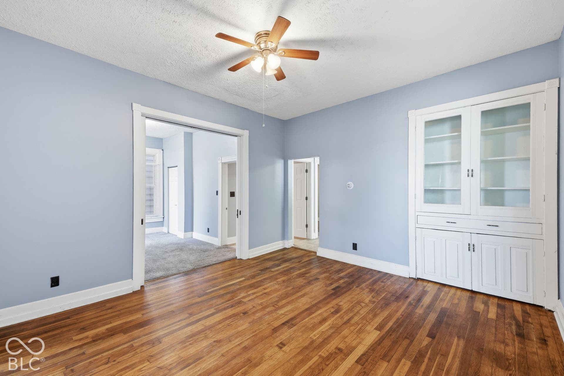 Hardwood flooring, painted walls, ceiling fan with light fixture, built-in display cabinetry, and painted trim work