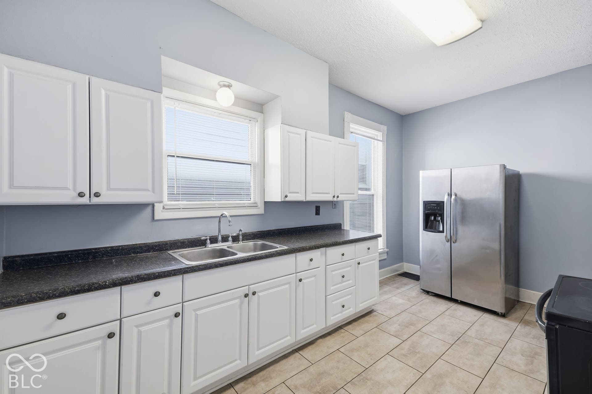 White cabinetry with dark hardware, dark countertops, and a dual stainless steel sink