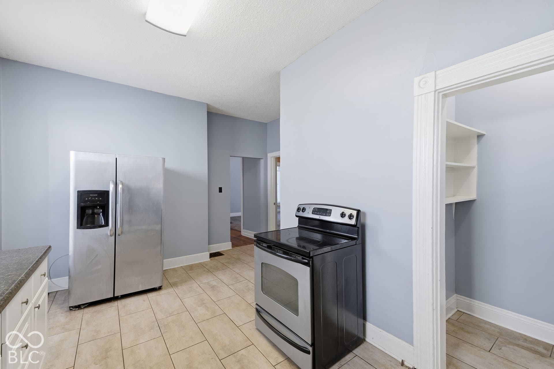 Stainless steel side-by-side refrigerator, stainless steel electric range, tile flooring, built-in shelving, and white trim