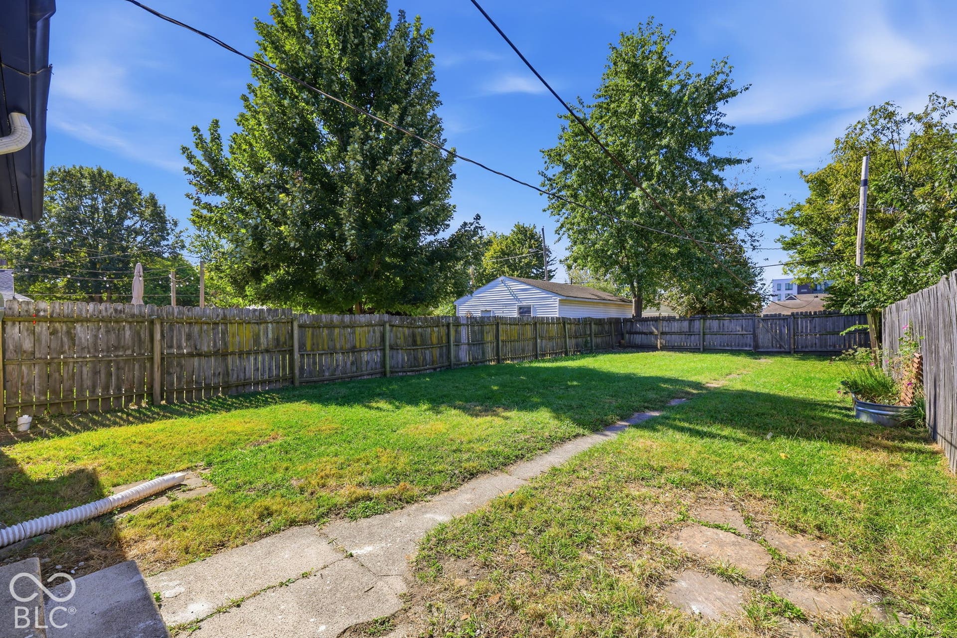 Expansive fenced backyard with a manicured lawn, concrete pathway, and mature trees