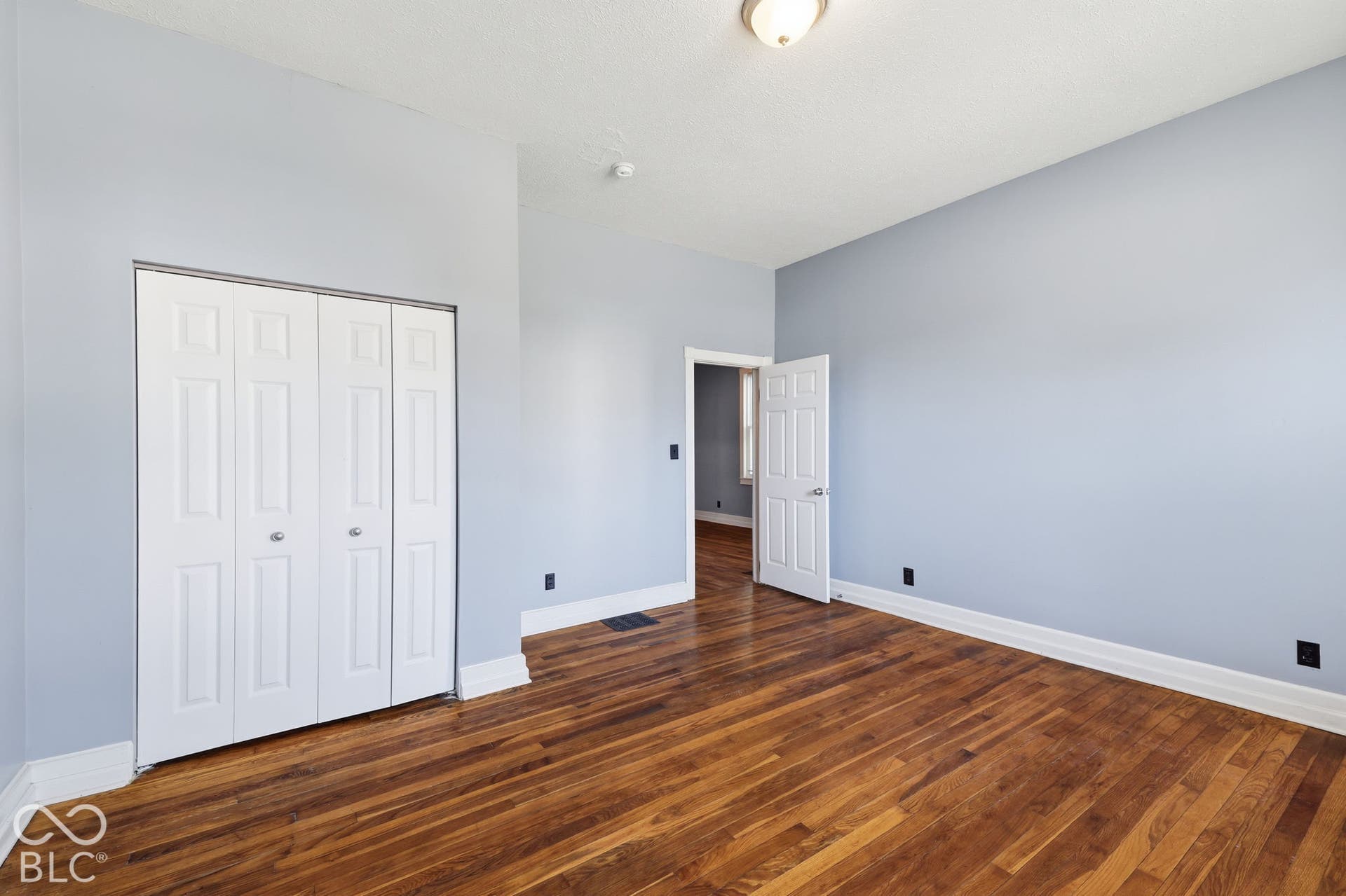 Hardwood flooring, painted walls, white trim, bi-fold closet doors, and a ceiling-mounted light fixture