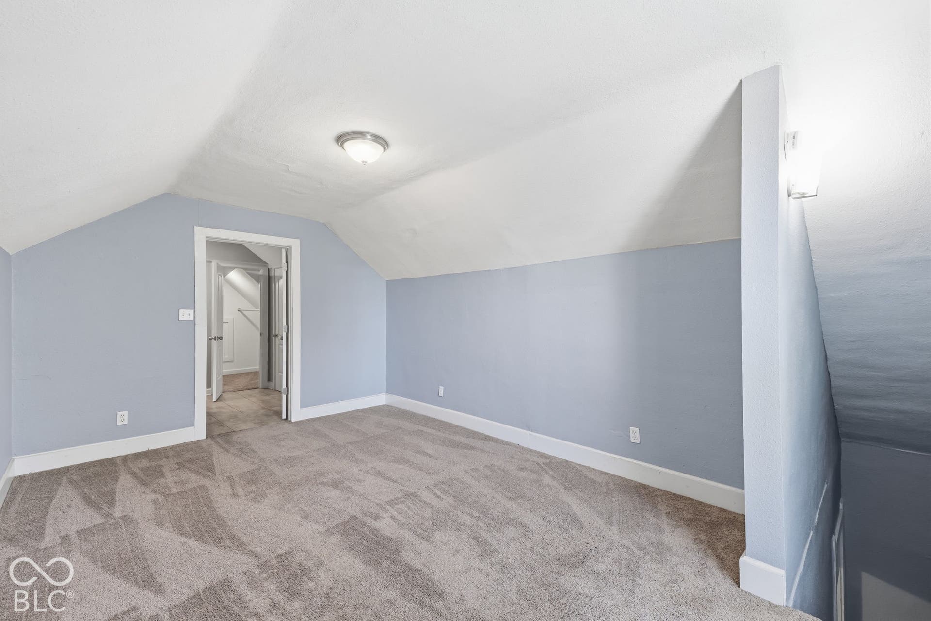 Vaulted ceiling with a flush-mount light fixture, gray patterned carpeting, and white baseboards