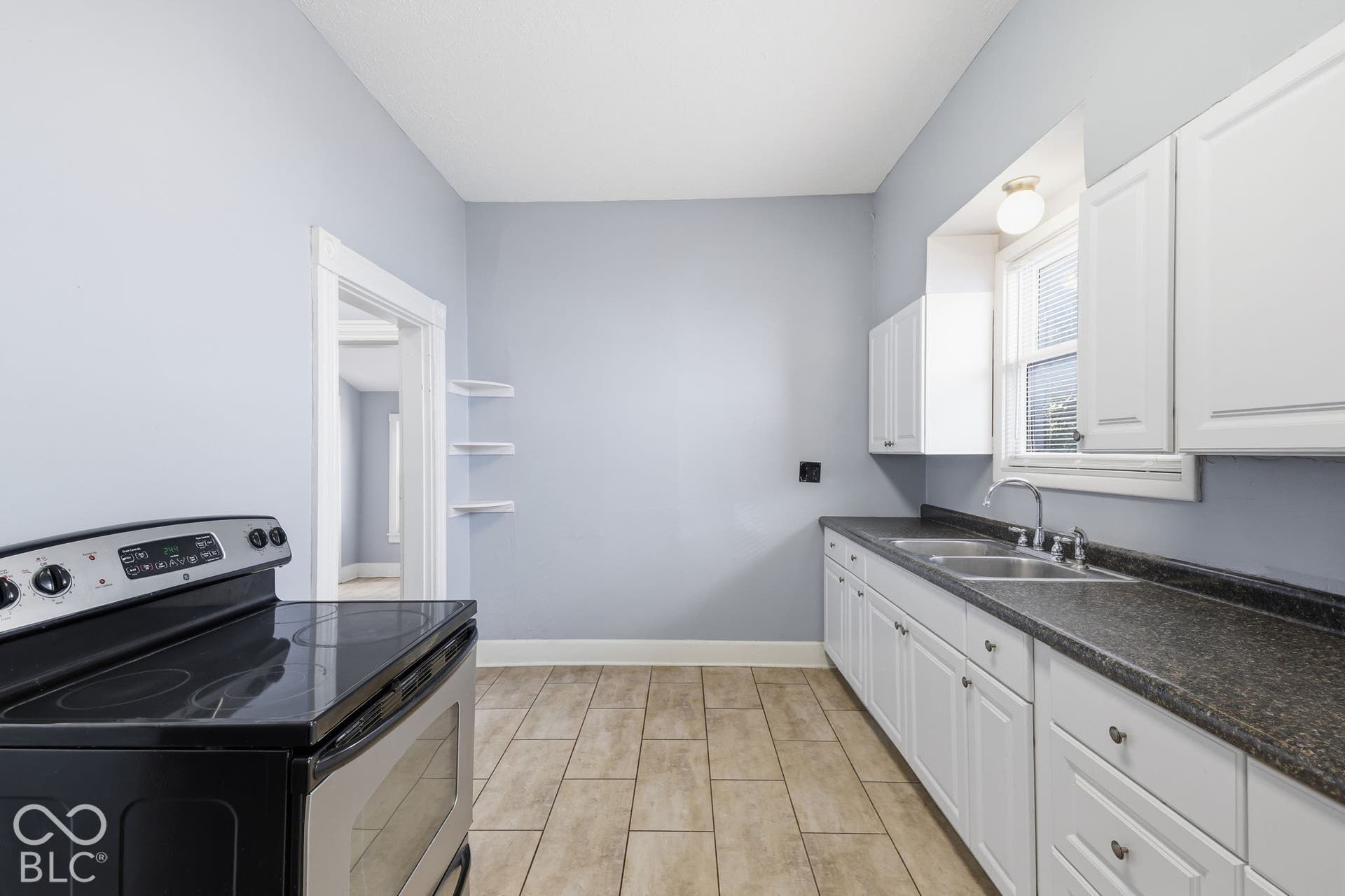 Kitchen featuring a black electric range, dual basin stainless steel sink, white cabinetry, dark countertops, and tile flooring