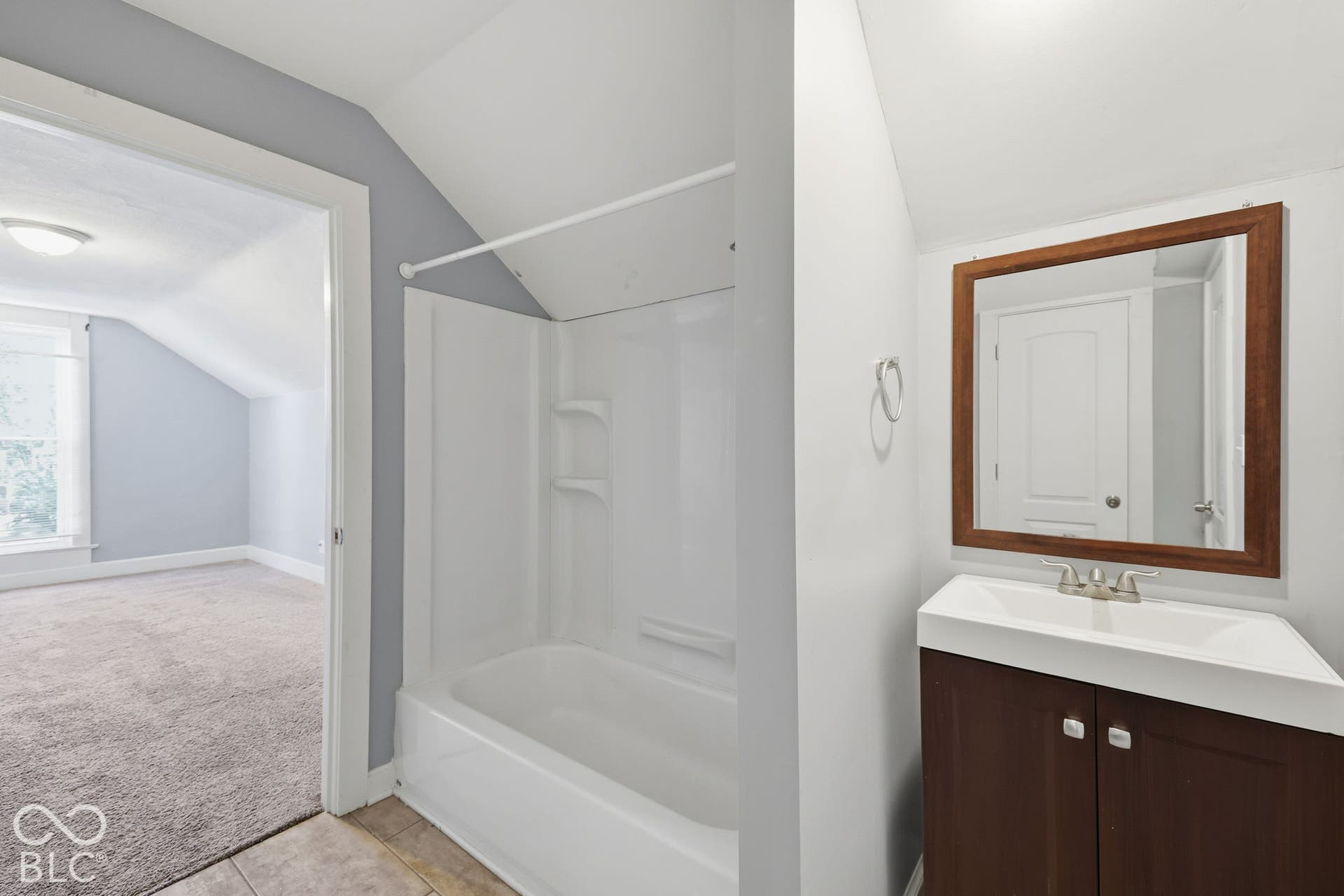 Bathroom featuring a white bathtub, wood-finish vanity with an integrated sink, and a framed mirror