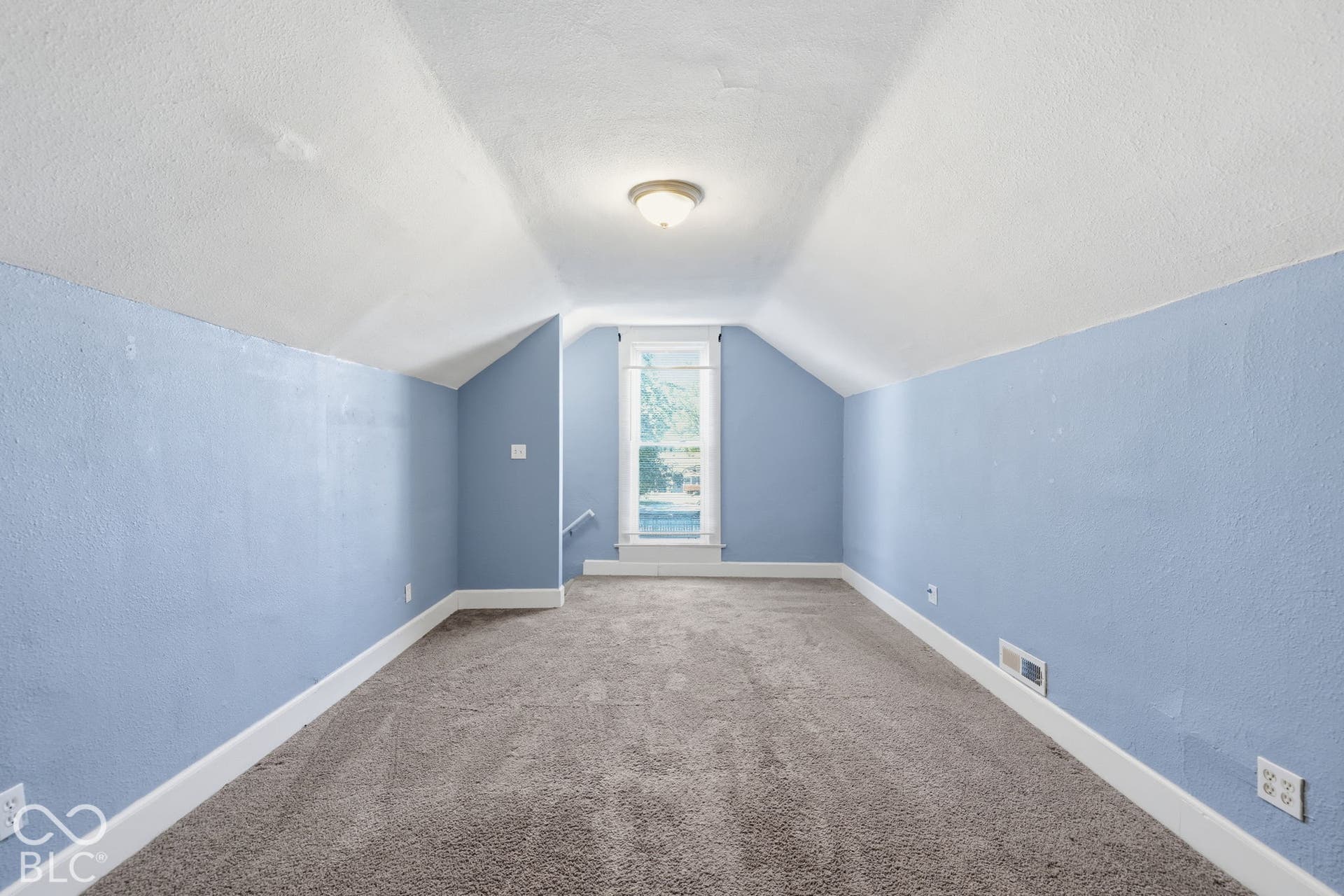 Vaulted ceiling room with textured blue walls, light carpet flooring, and a single window