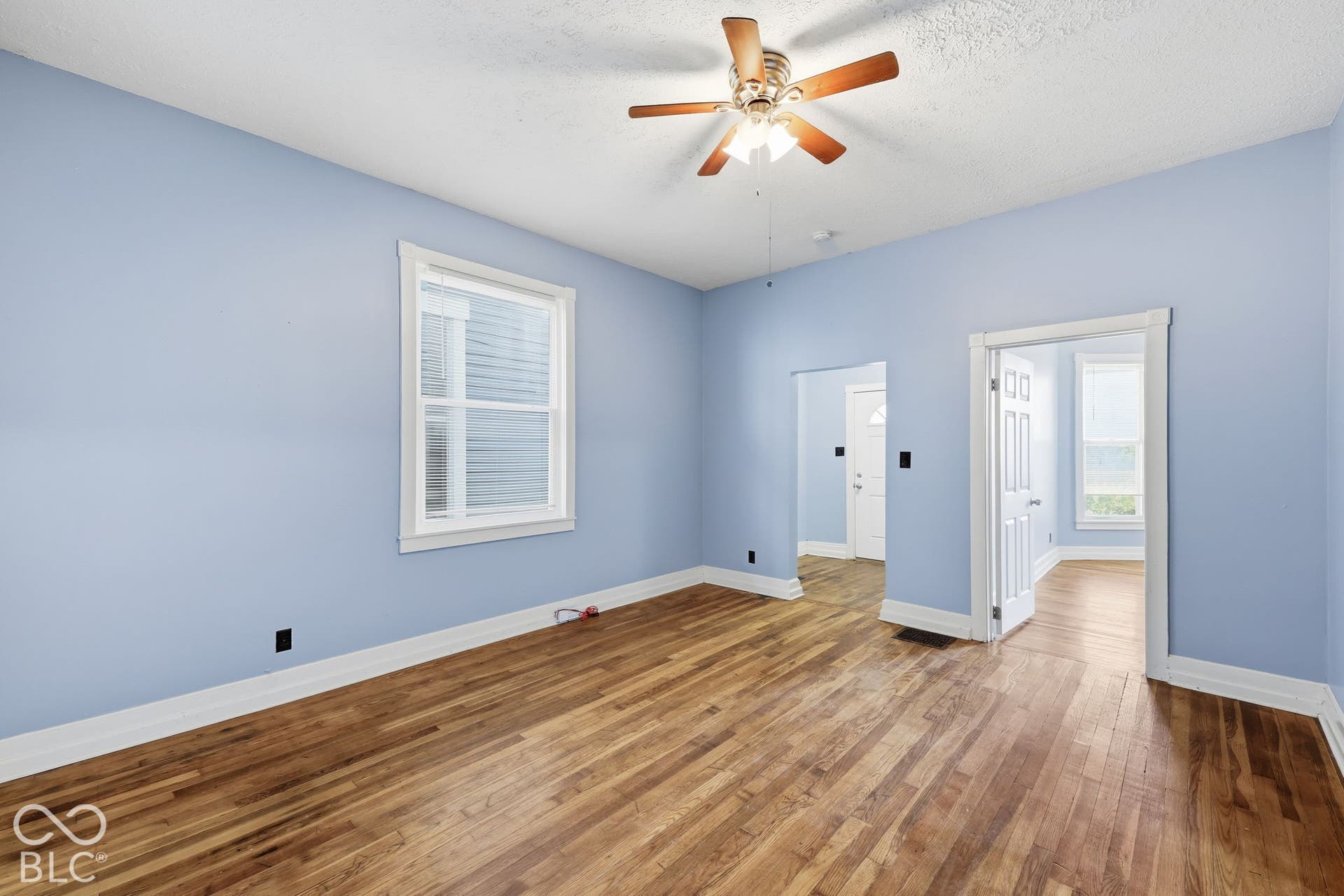 Wood-finish flooring, white trim, recessed window with blinds, and a ceiling fan with light fixture
