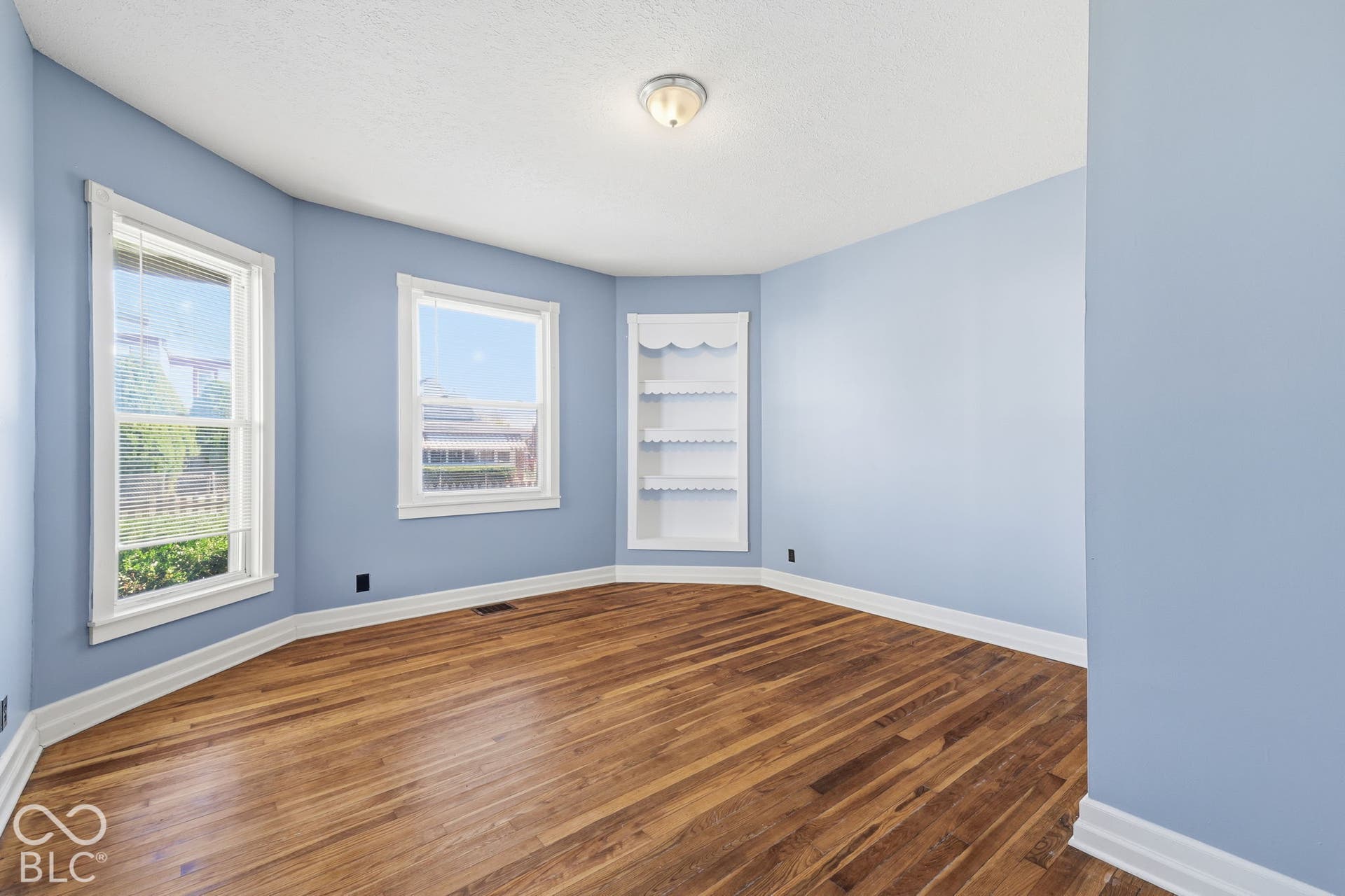 Hardwood flooring with a bay window design, built-in shelving, and a semi-flush ceiling light